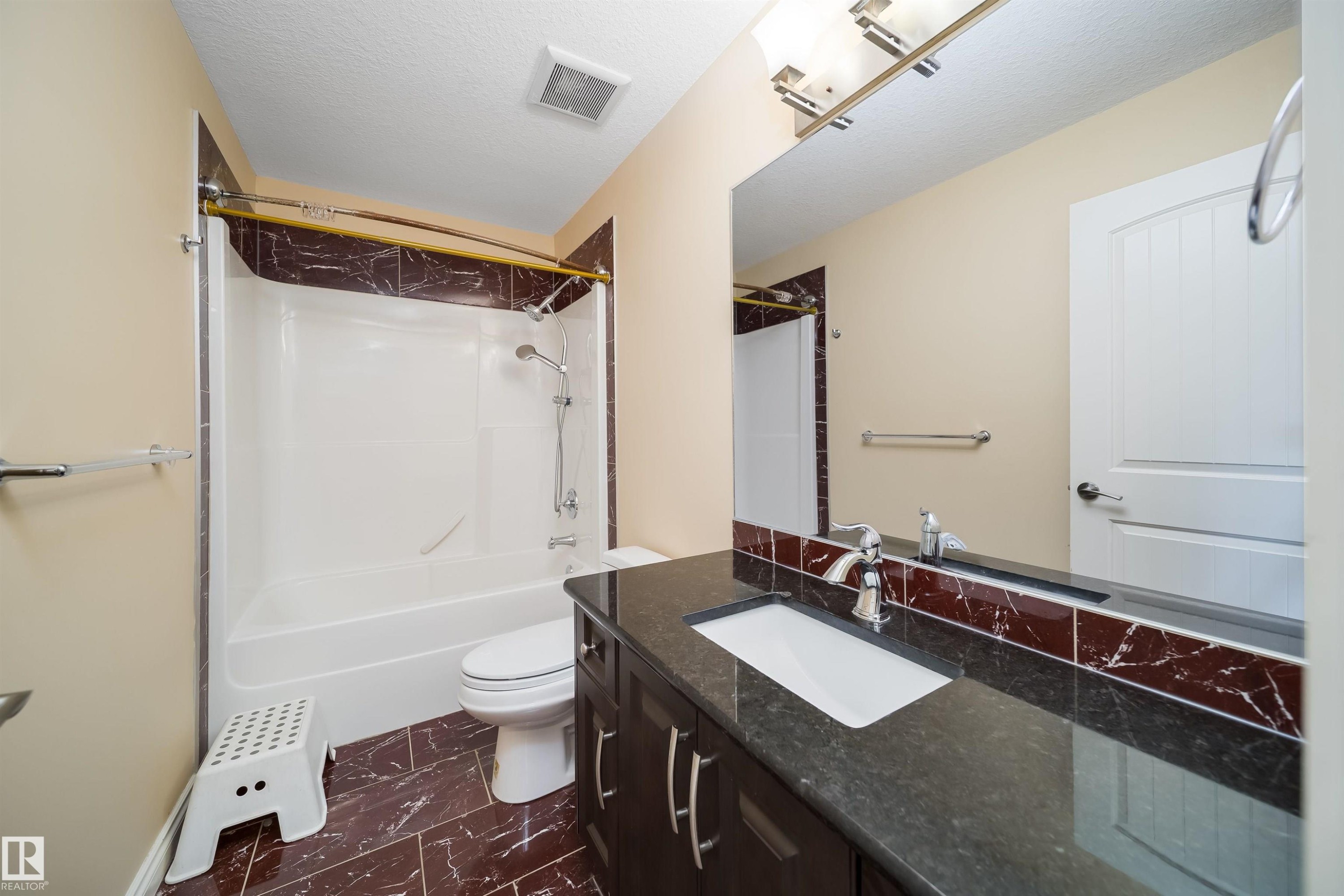 Full bathroom featuring a dark wood-finish vanity with a dark countertop and integrated sink, a large mirror, a shower-over-tub combination with a curved shower rod, and brown tile flooring - 1508 Cunningham Cape Cape, Edmonton, AB - Indoor Photo Showing Bathroom