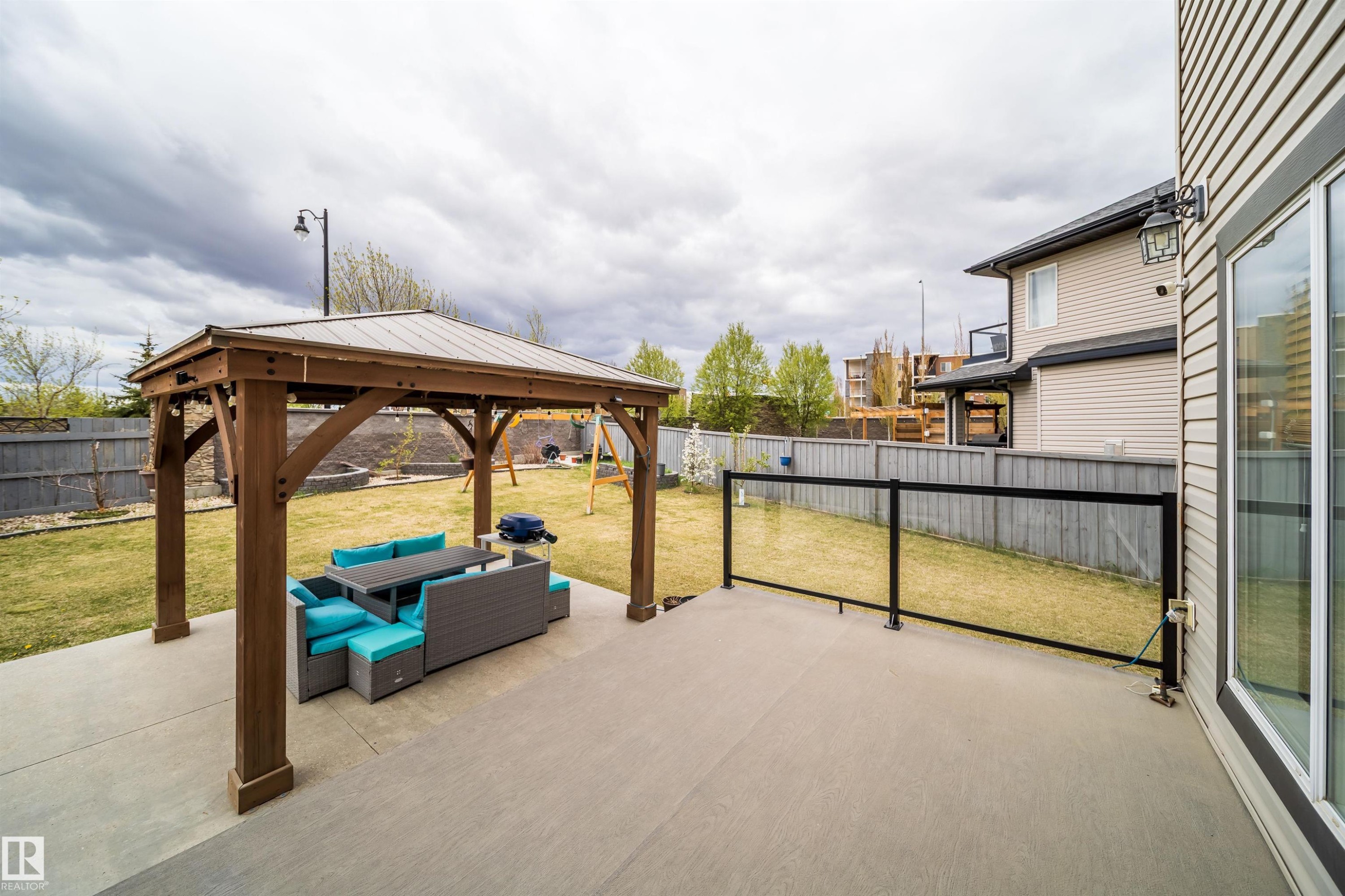 Expansive concrete patio featuring a wood gazebo with a metal roof, glass railing, and a sliding glass door entry to the home - 1508 Cunningham Cape Cape, Edmonton, AB - Outdoor With Exterior