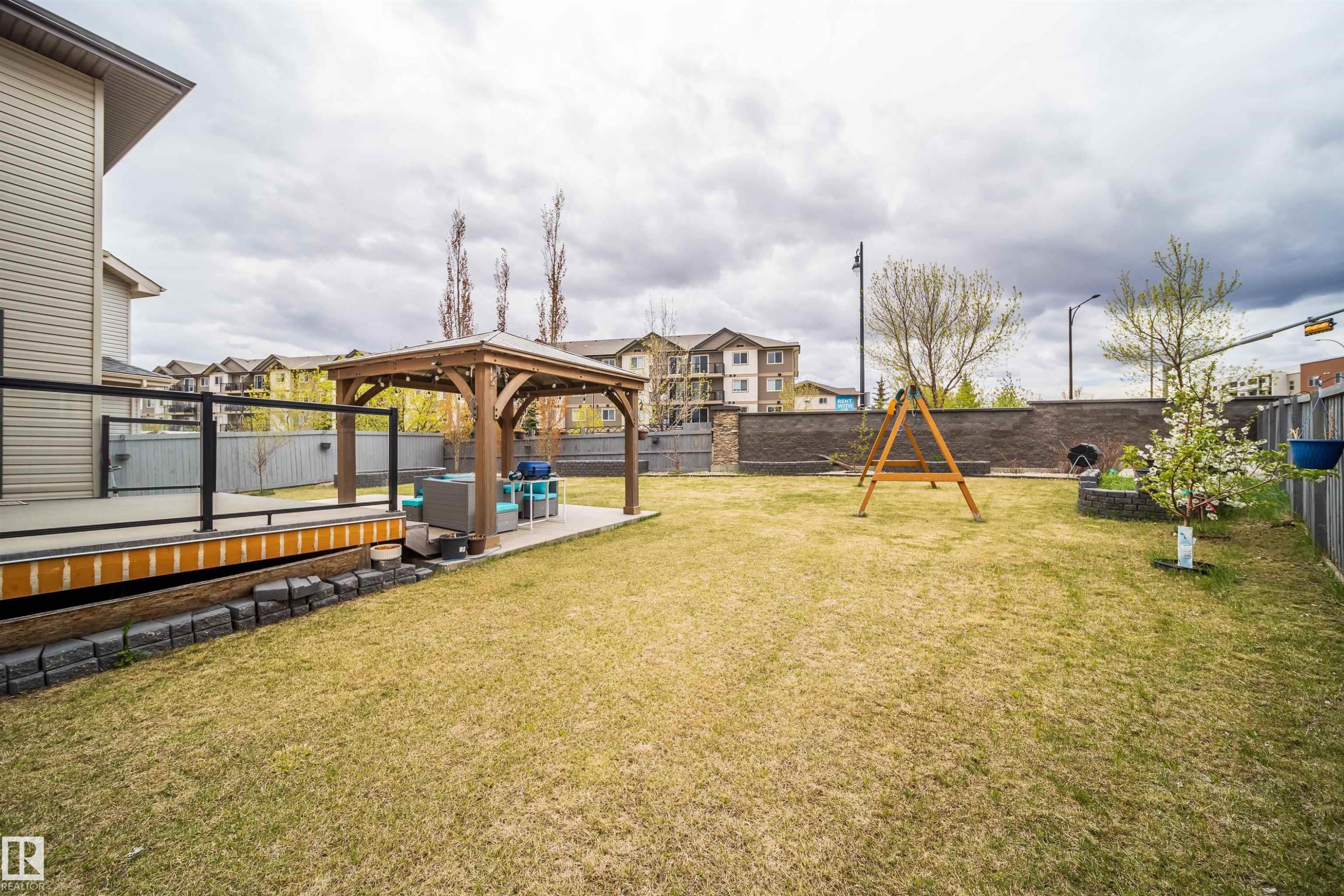 Expansive backyard featuring a built-in wooden deck with glass railing, a paved patio, and a freestanding pergola - 1508 Cunningham Cape Cape, Edmonton, AB - Outdoor
