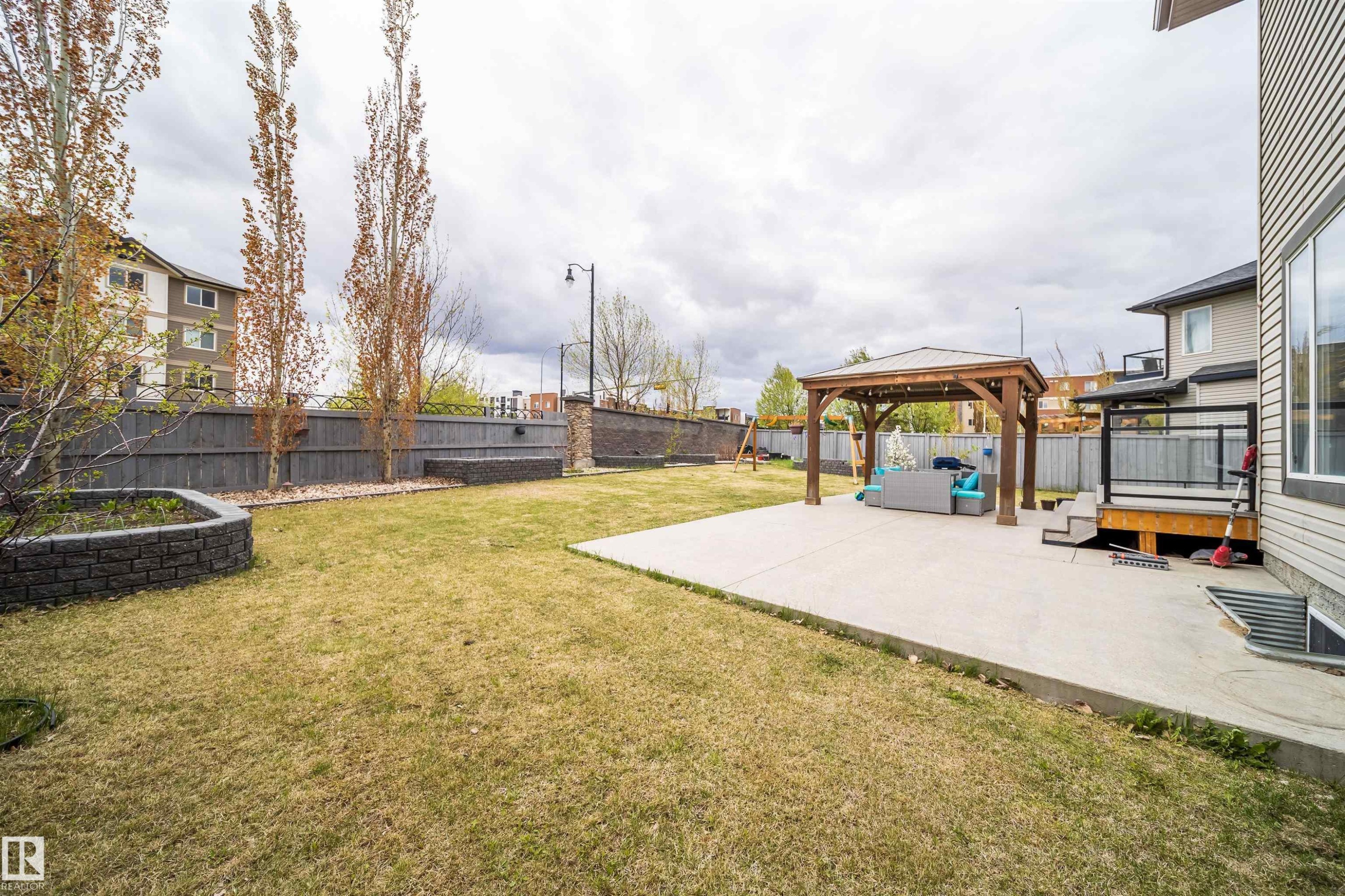 Spacious backyard featuring a concrete patio, wooden gazebo, expansive lawn area, and a tiered deck with glass railings - 1508 Cunningham Cape Cape, Edmonton, AB - Outdoor