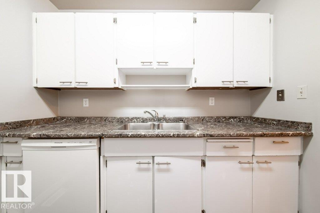 Kitchen area with white cabinetry, a double basin stainless steel sink, a stainless steel faucet, and a white dishwasher - 17106 108 St Nw, Edmonton, AB - Indoor Photo Showing Kitchen With Double Sink