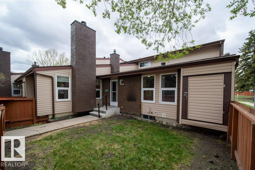Rear exterior featuring light beige siding, exposed brick accents, and a prominent brown chimney structure - 17106 108 St Nw, Edmonton, AB - Outdoor