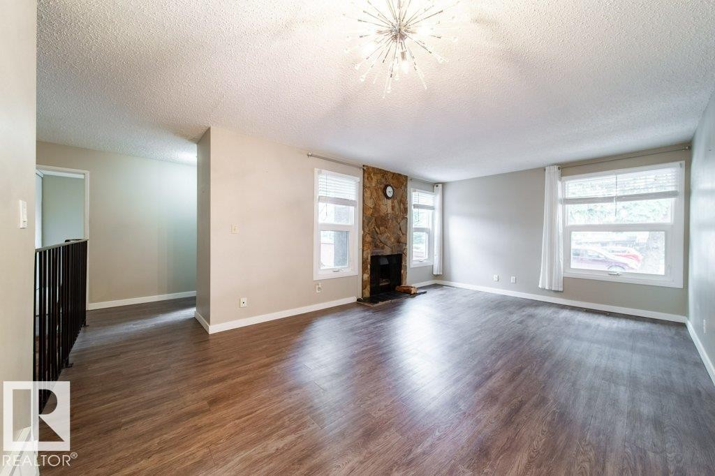 Spacious living area featuring wood-finish flooring, a stone-clad fireplace, and multiple windows - 17106 108 St Nw, Edmonton, AB - Indoor Photo Showing Living Room With Fireplace