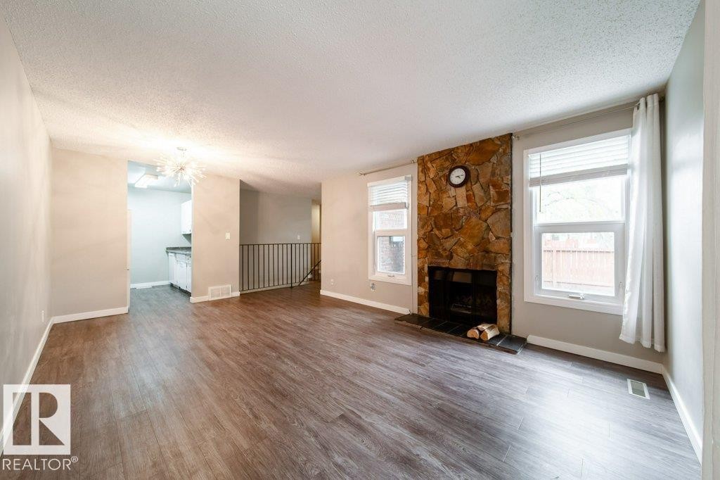 Living area featuring wood-finish flooring and a stone-clad fireplace with a dark hearth - 17106 108 St Nw, Edmonton, AB - Indoor Photo Showing Living Room With Fireplace