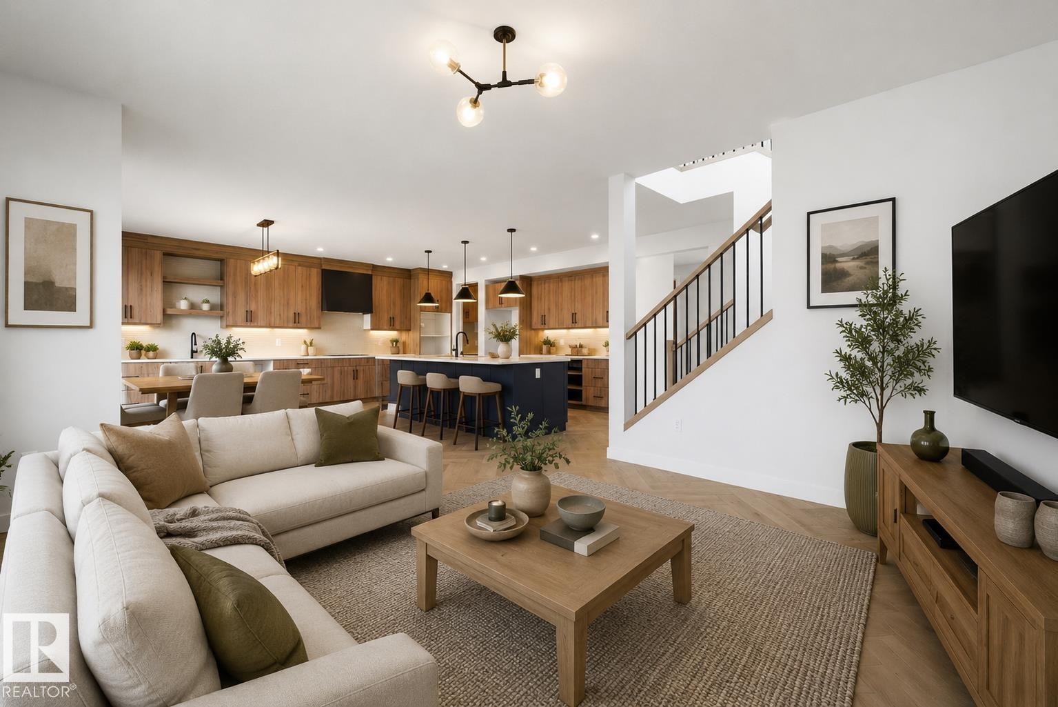 Open-concept living area featuring herringbone wood-finish flooring, a contemporary chandelier, a kitchen with wood cabinetry and a dark-toned island with pendant lighting, and a staircase with black metal balusters - 17108 2 Street, Edmonton, AB - Indoor Photo Showing Living Room