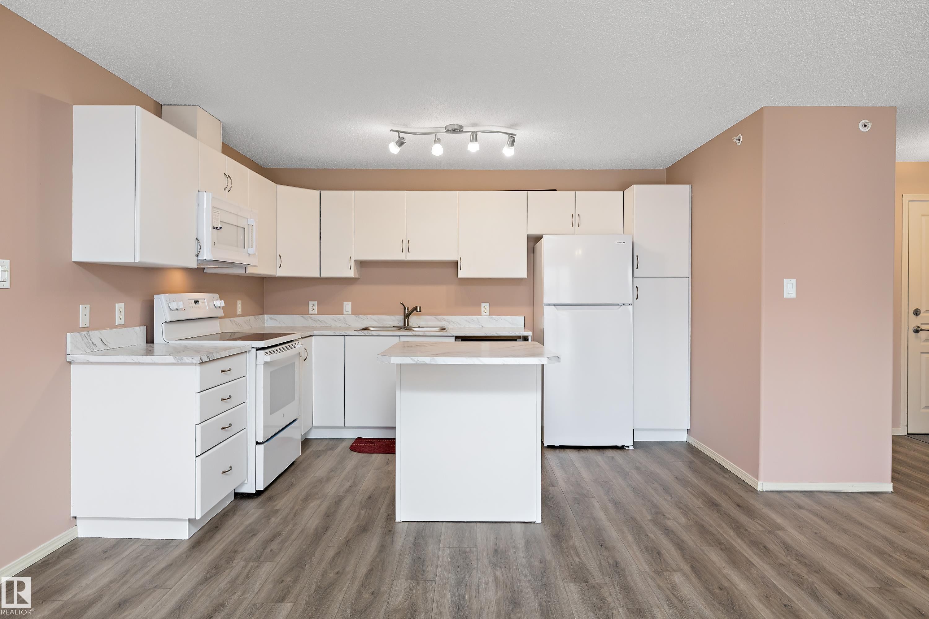 White kitchen cabinetry with integrated appliances, light-toned countertops, and wood-finish flooring - 406 16035 132 Street, Edmonton, AB - Indoor Photo Showing Kitchen