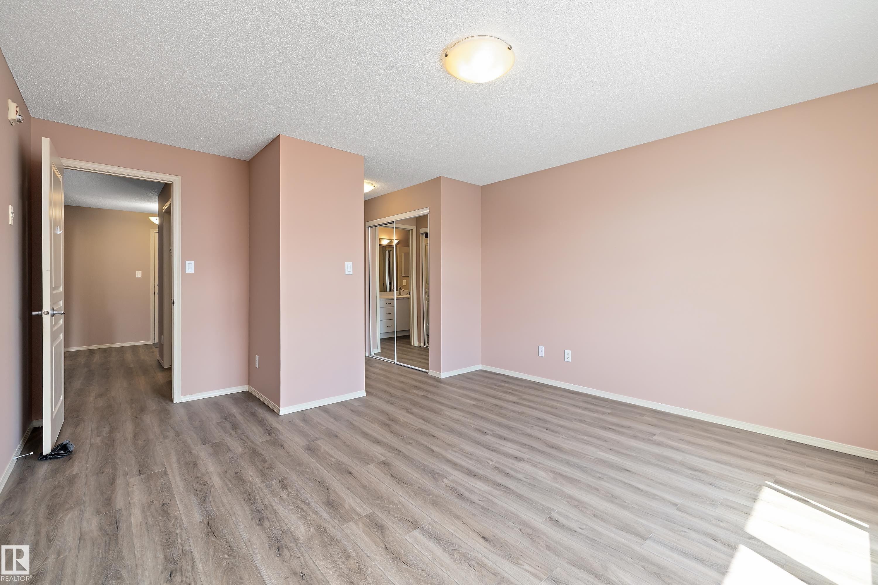 Spacious room with wood-finish flooring, a contemporary ceiling light fixture, and light-toned wall paint - 406 16035 132 Street, Edmonton, AB - Indoor Photo Showing Other Room