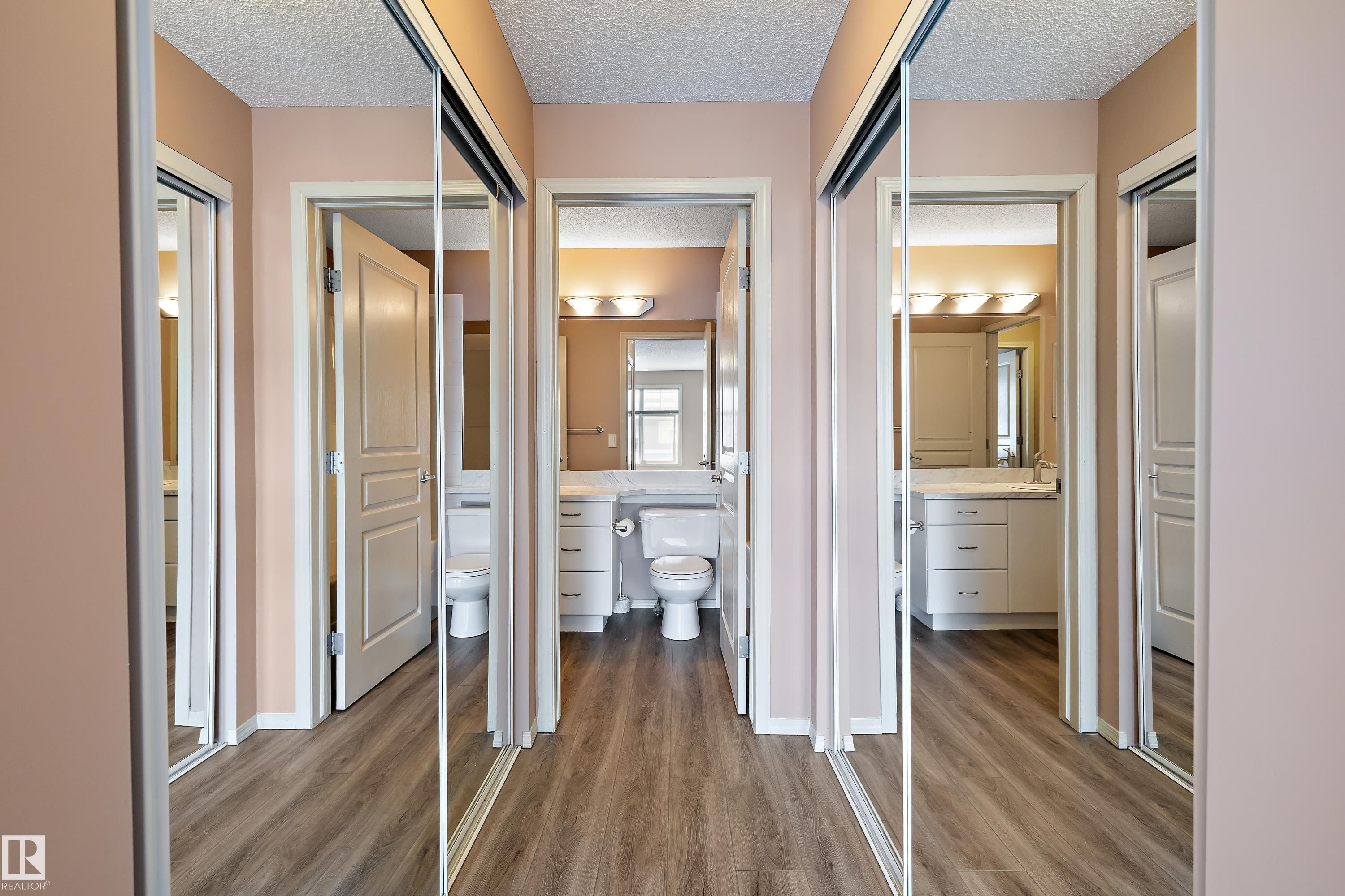 Hallway featuring wood-finish flooring, mirrored sliding closet doors, and light-toned walls - 406 16035 132 Street, Edmonton, AB - Indoor Photo Showing Other Room