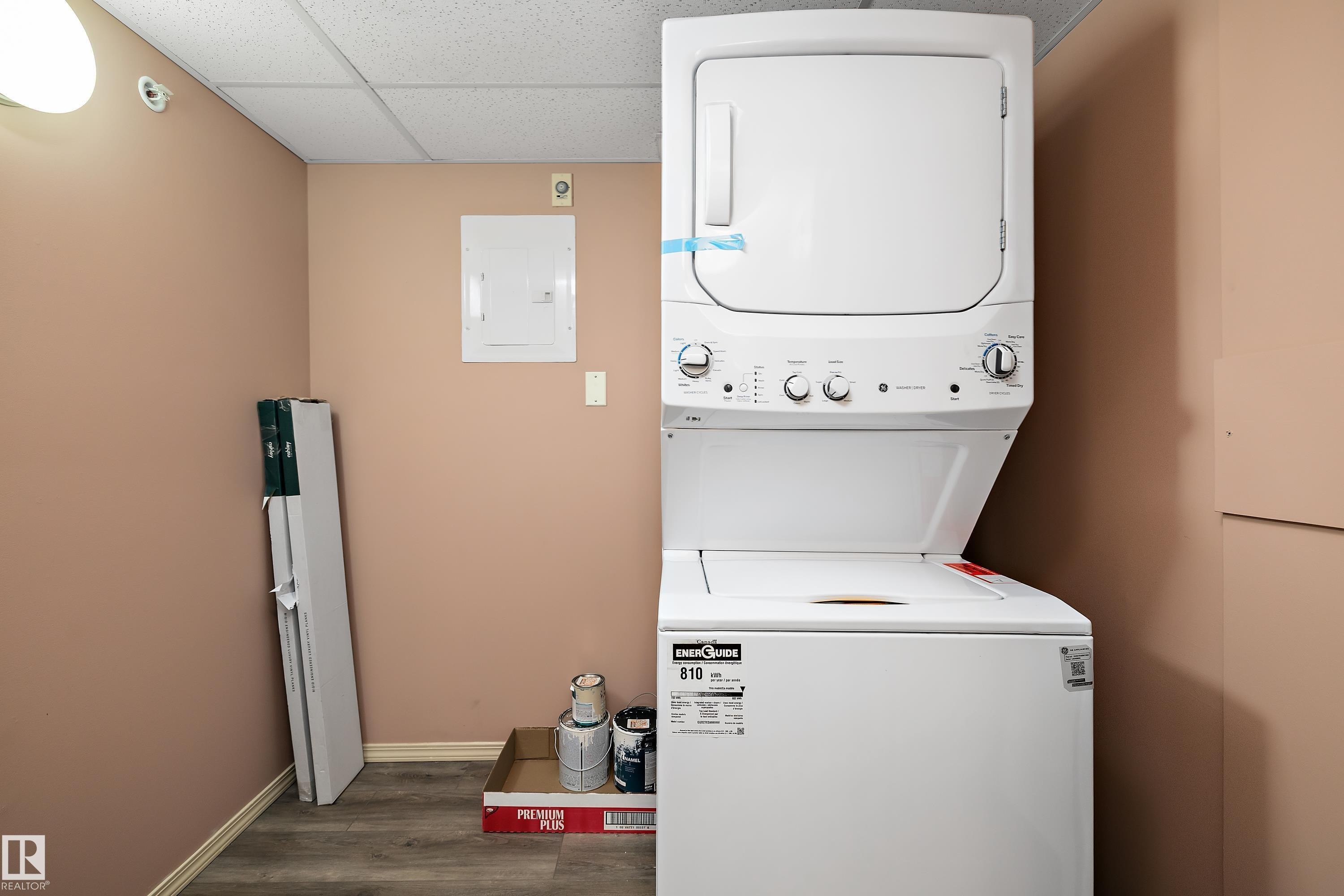 Dedicated laundry area featuring a white stacked washer and dryer unit, neutral wall paint, and wood-finish flooring - 406 16035 132 Street, Edmonton, AB - Indoor Photo Showing Laundry Room