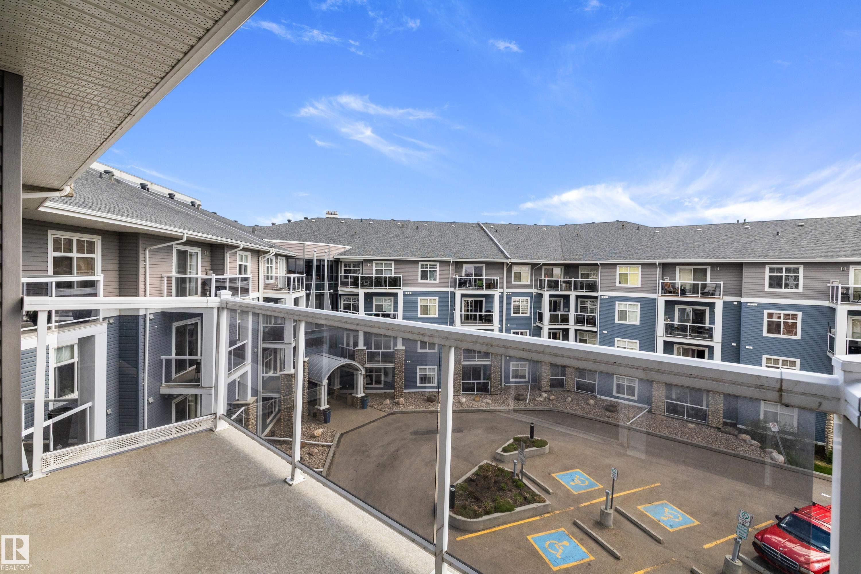 Private balcony with glass panel railing and concrete flooring overlooking a multi-story residential building with a central courtyard - 406 16035 132 Street, Edmonton, AB - Outdoor With Balcony With Exterior