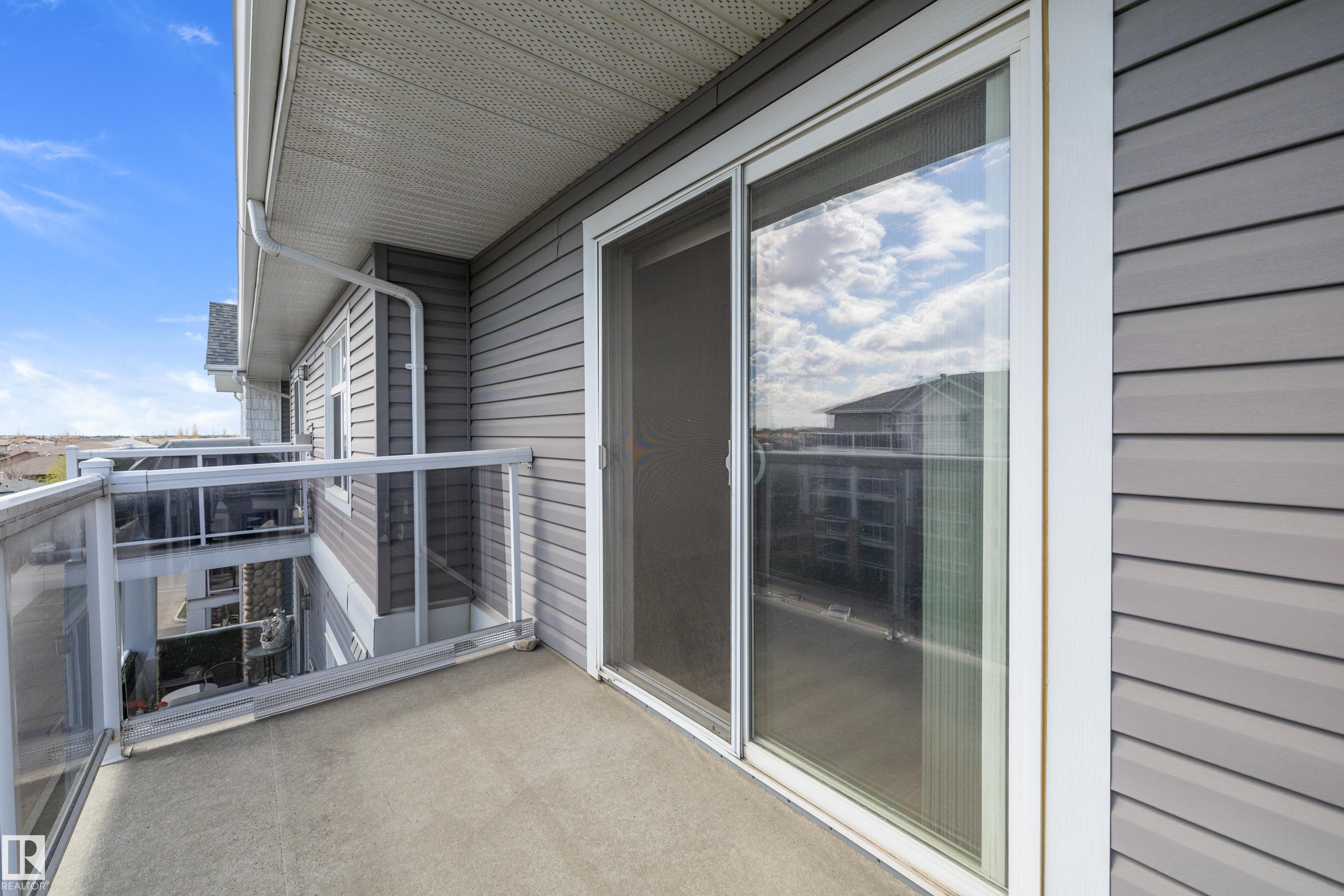 Private balcony featuring a concrete surface, glass and white railing, and grey horizontal siding - 406 16035 132 Street, Edmonton, AB - Outdoor With Balcony With Deck Patio Veranda With Exterior