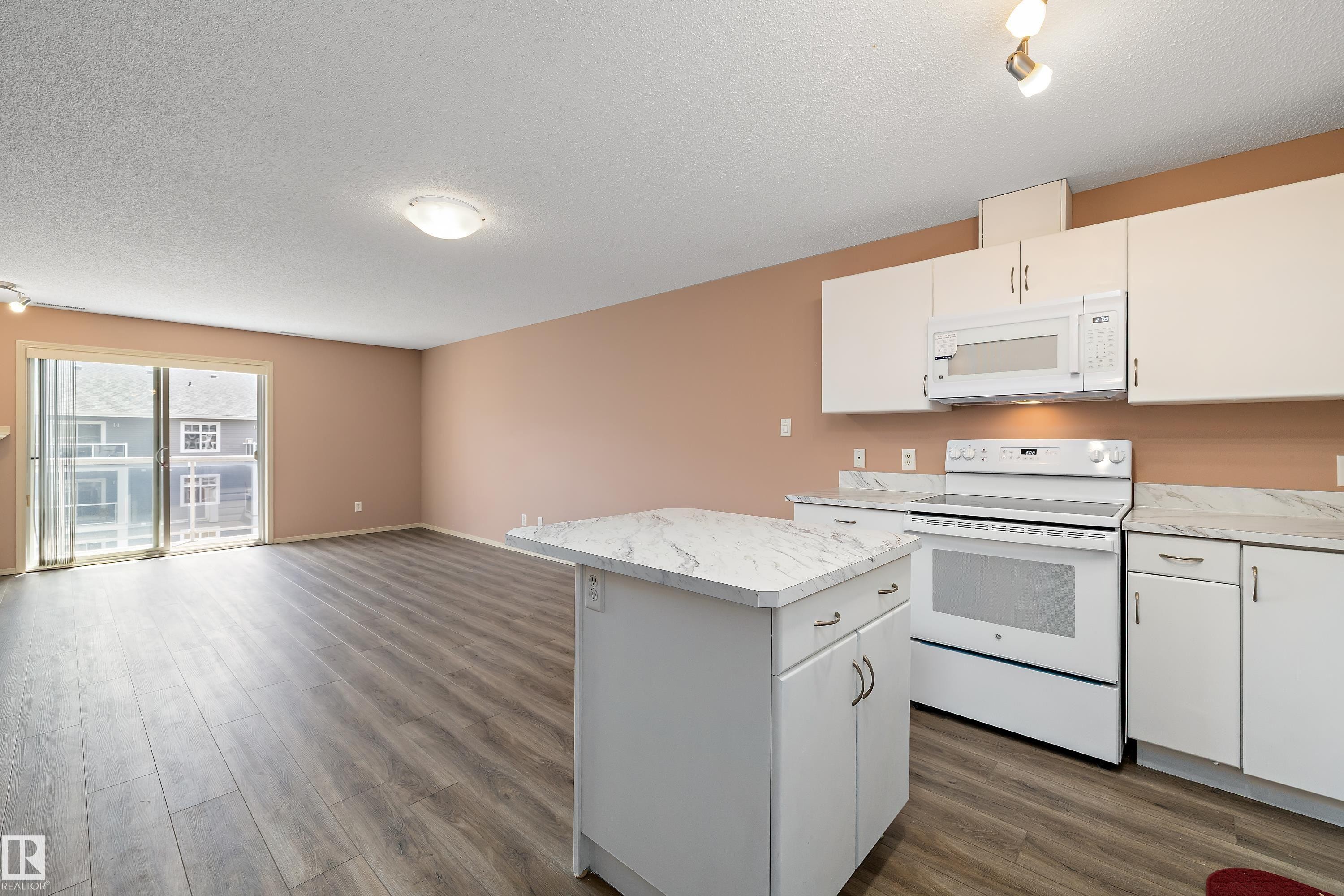 Kitchen area with white cabinetry, a white electric range, and a built-in microwave - 406 16035 132 Street, Edmonton, AB - Indoor Photo Showing Kitchen