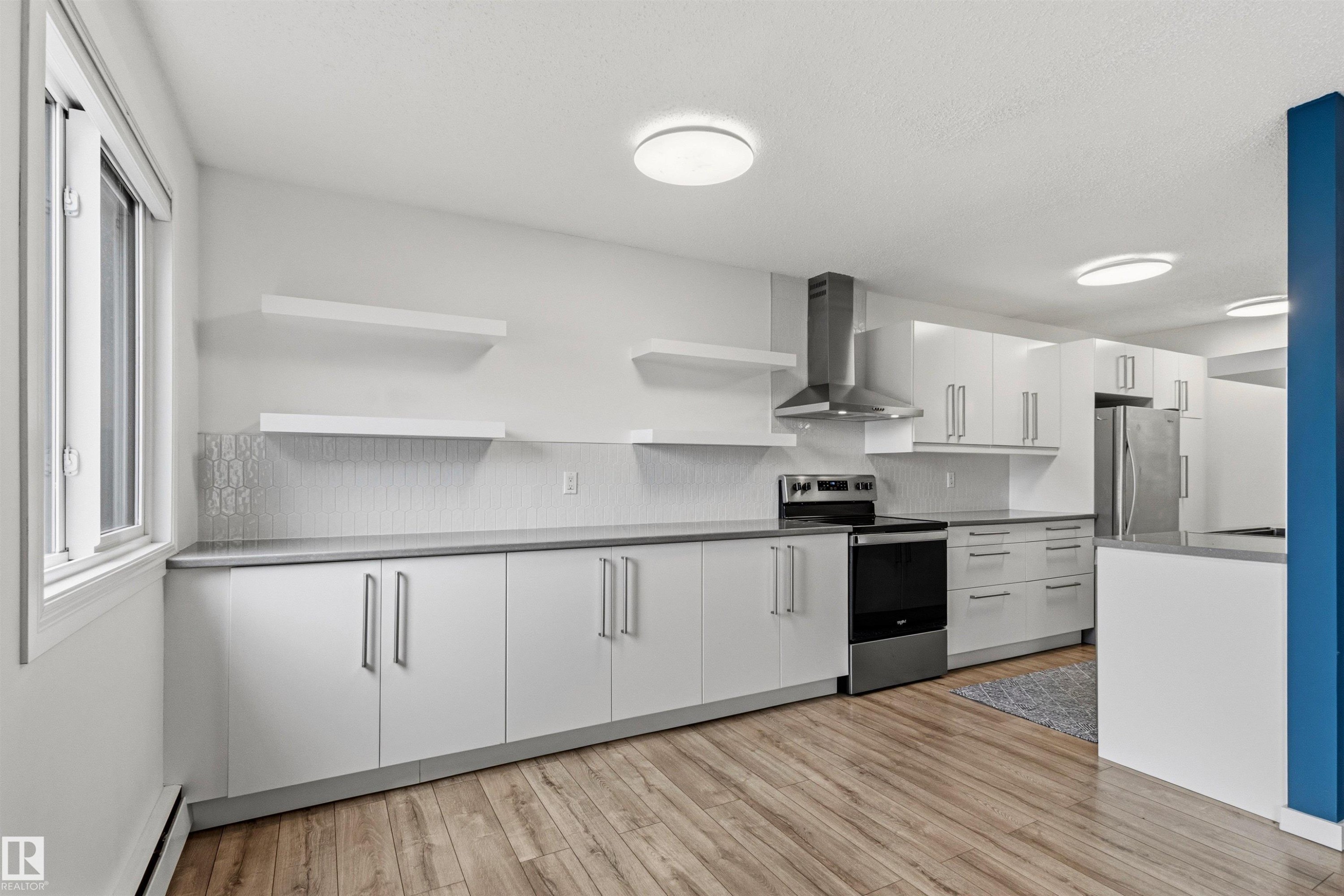 Modern kitchen featuring wood-finish flooring, white cabinetry with brushed nickel hardware, and stainless steel appliances - 217 14819 51 Avenue, Edmonton, AB