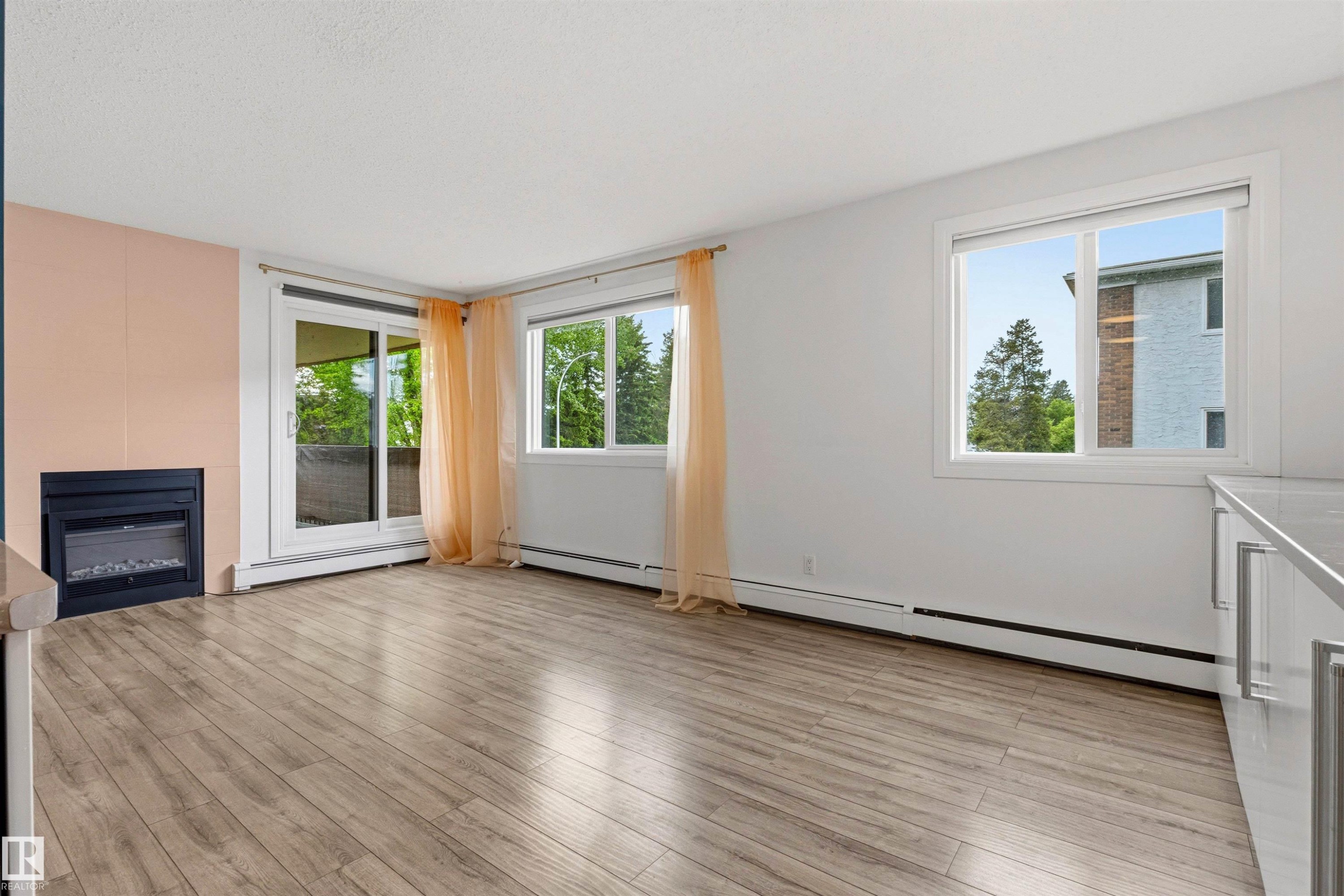 Living area featuring wood-finish flooring, a built-in fireplace, and abundant natural light from multiple windows and a sliding glass door - 217 14819 51 Avenue, Edmonton, AB