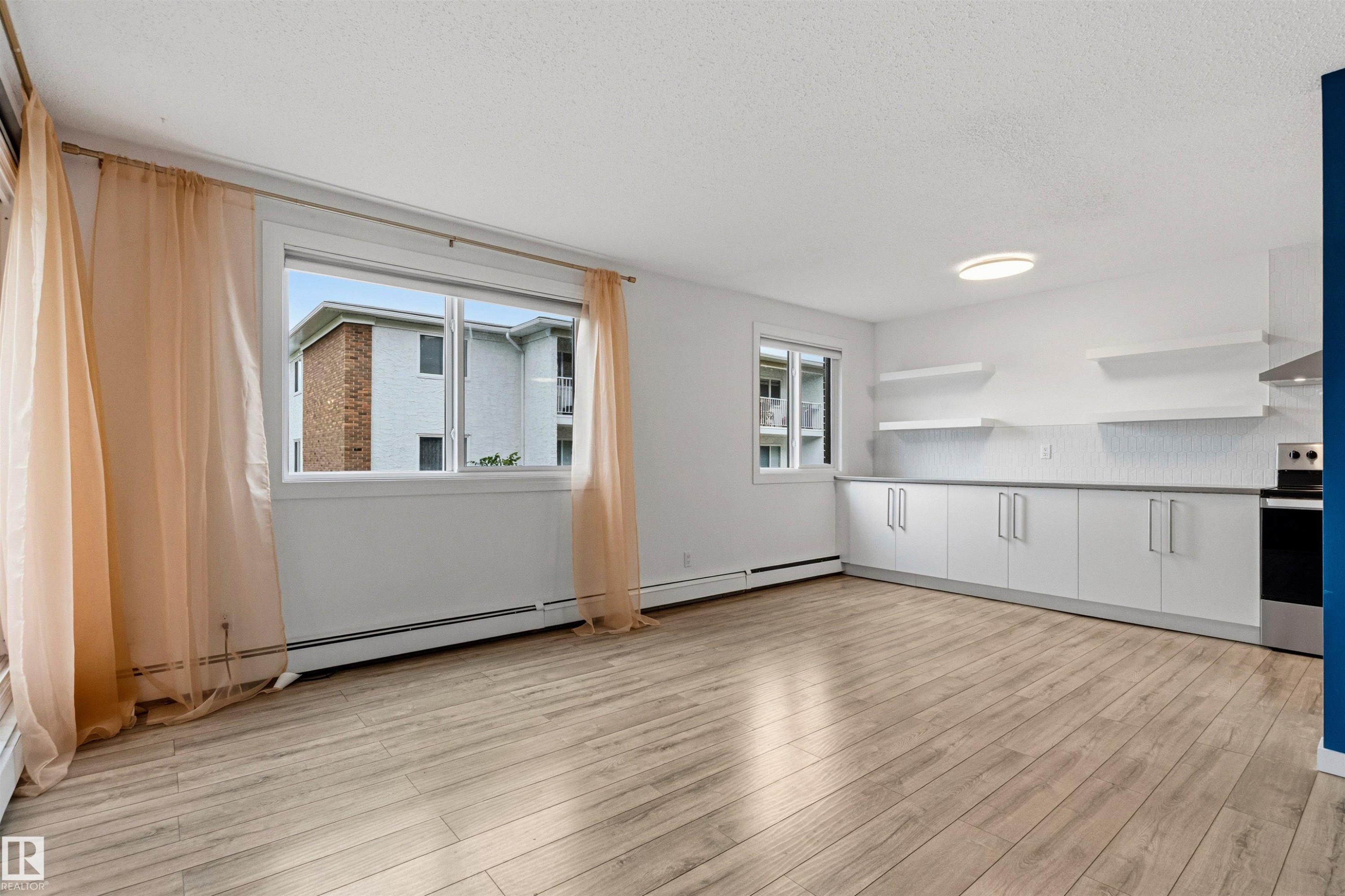 Open-concept living area with wood-finish flooring, large windows, and contemporary overhead lighting - 217 14819 51 Avenue, Edmonton, AB