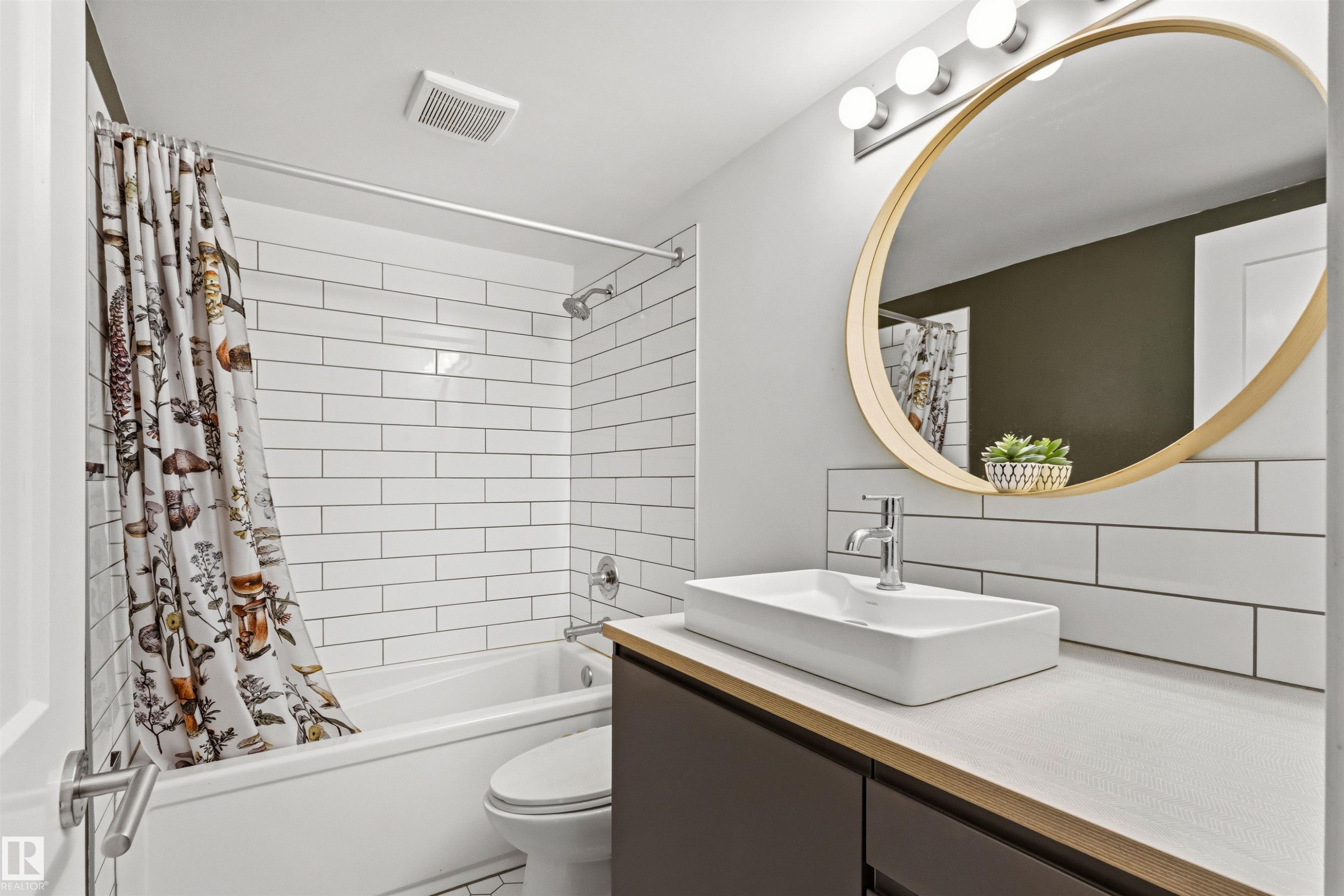 Full bathroom featuring a rectangular vessel sink with chrome faucet, a large round mirror, and a built-in bathtub with subway tile surround - 217 14819 51 Avenue, Edmonton, AB