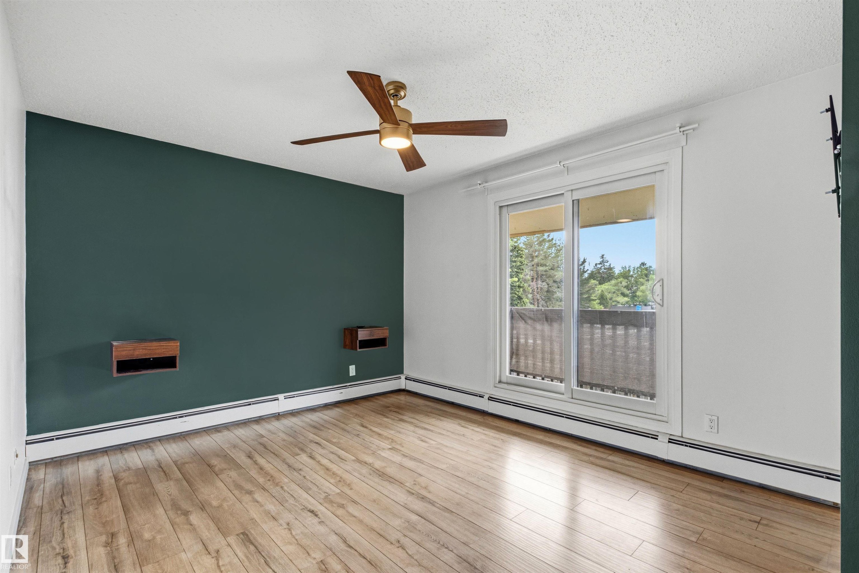 Room featuring wood-finish flooring, a ceiling fan with integrated lighting, and a sliding glass door leading to a balcony - 217 14819 51 Avenue, Edmonton, AB
