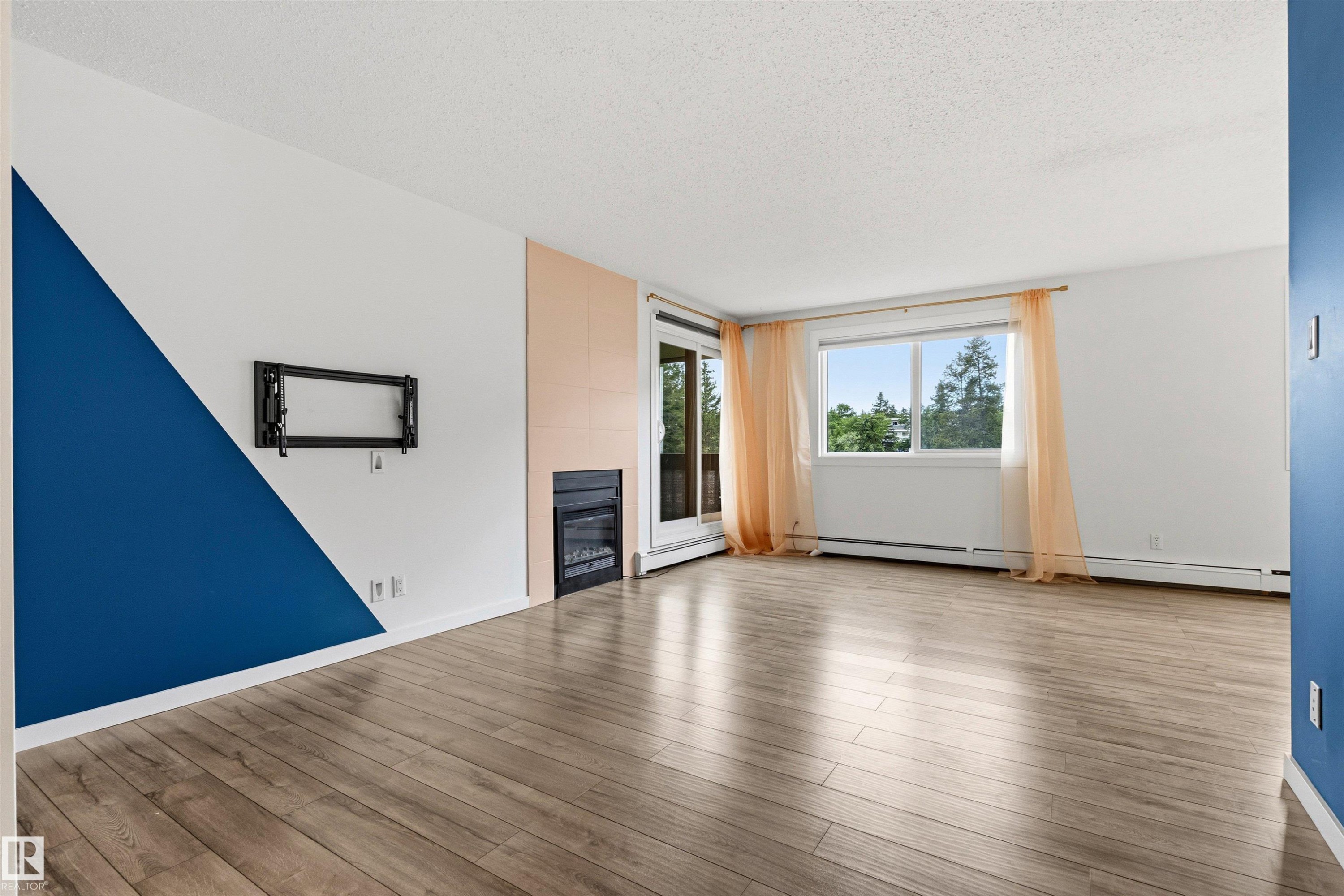 Spacious interior featuring wood-finish flooring, a contemporary accent wall, and a built-in fireplace - 217 14819 51 Avenue, Edmonton, AB