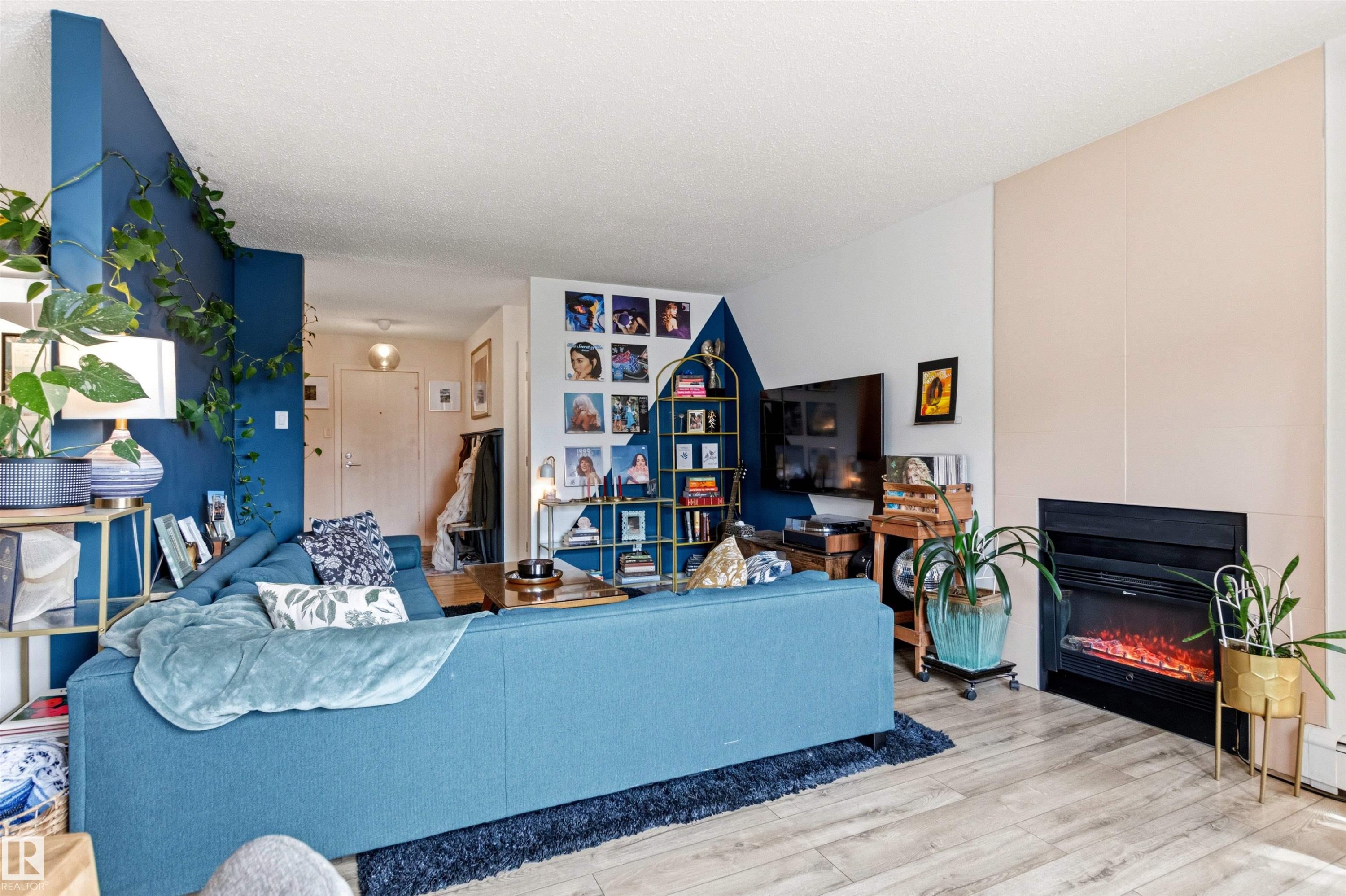 Living area featuring wood-finish flooring, a built-in fireplace with a dark surround, and a partial accent wall - 217 14819 51 Avenue, Edmonton, AB