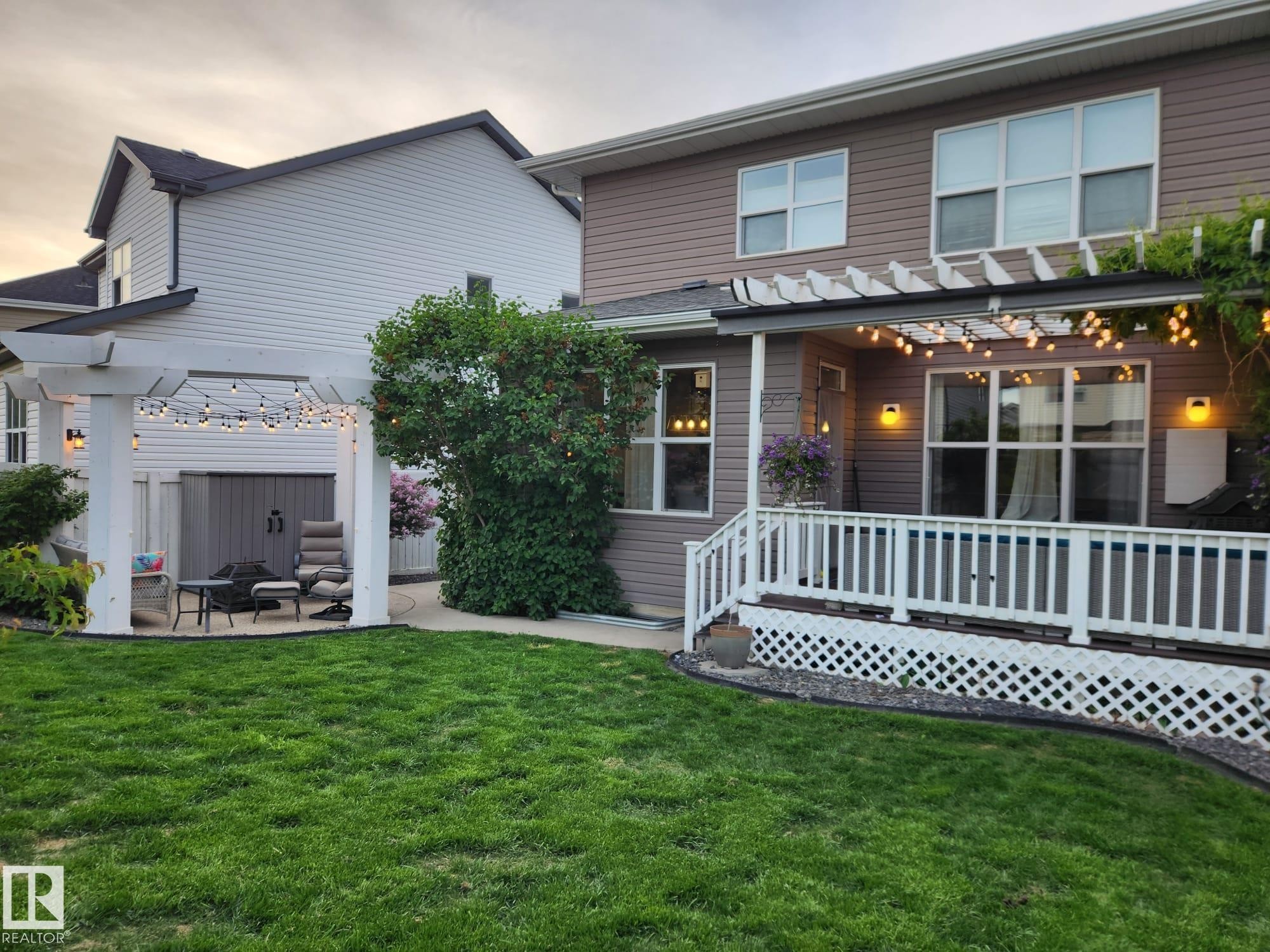 Expansive green lawn with a white lattice-skirted deck featuring a white railing and an overhead pergola - 22933 94A Avenue, Edmonton, AB - Outdoor With Deck Patio Veranda With Exterior