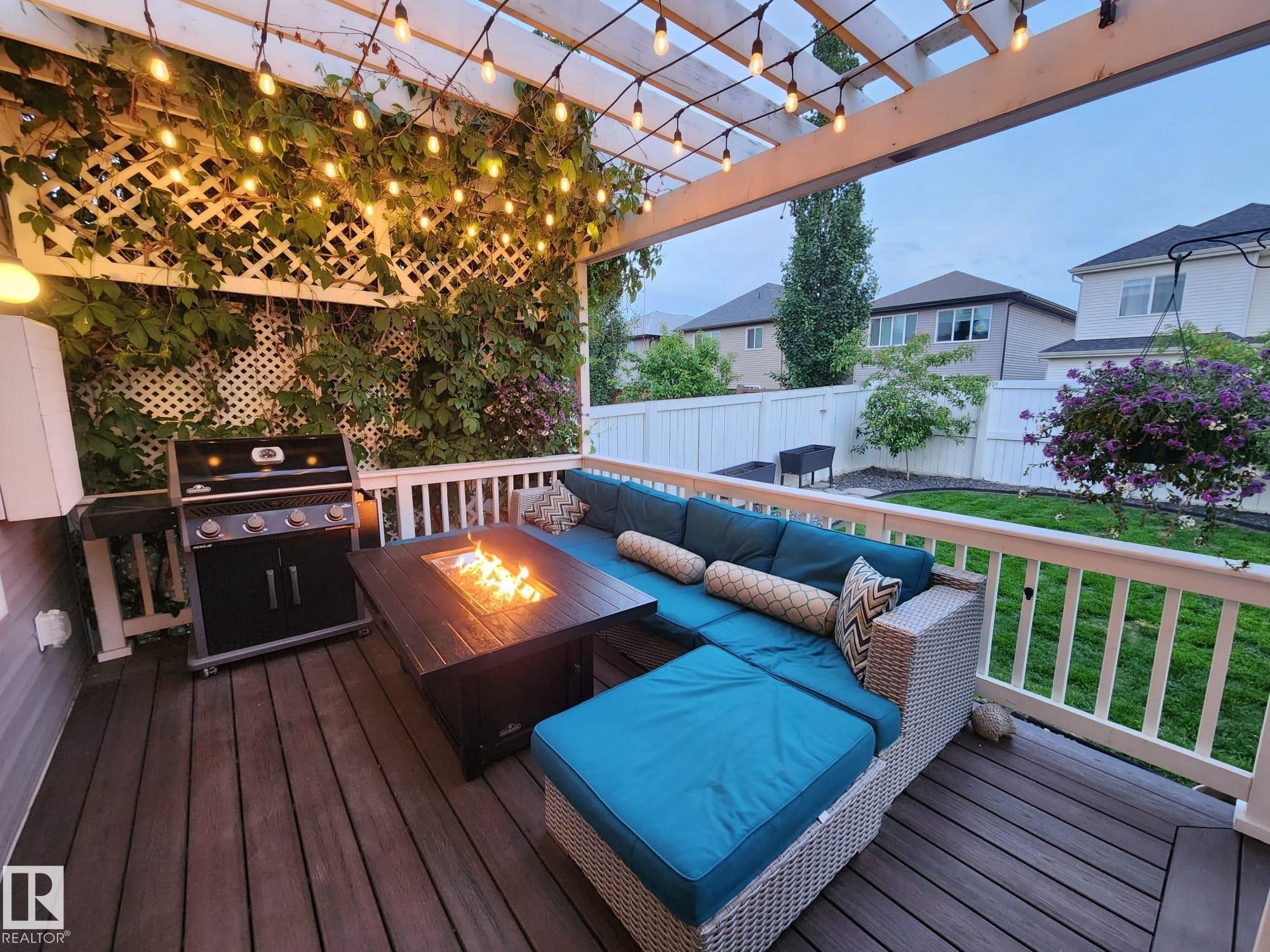Covered outdoor deck featuring composite decking, a white pergola with string lighting, and a lattice privacy screen with climbing greenery - 22933 94A Avenue, Edmonton, AB - Photo Showing Other Room