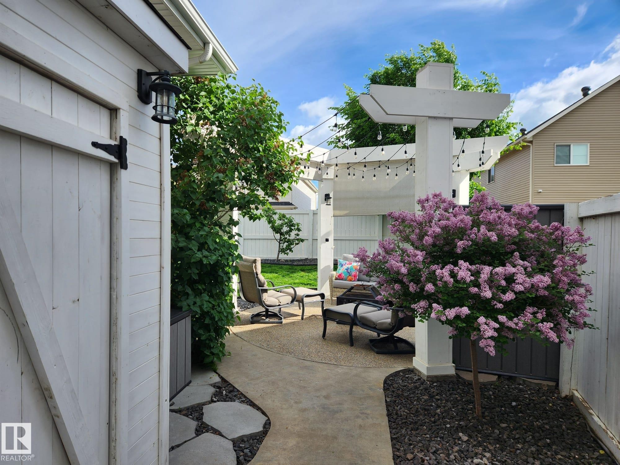 Backyard patio featuring a white pergola, concrete pathway, and mature landscaping - 22933 94A Avenue, Edmonton, AB - Outdoor With Deck Patio Veranda