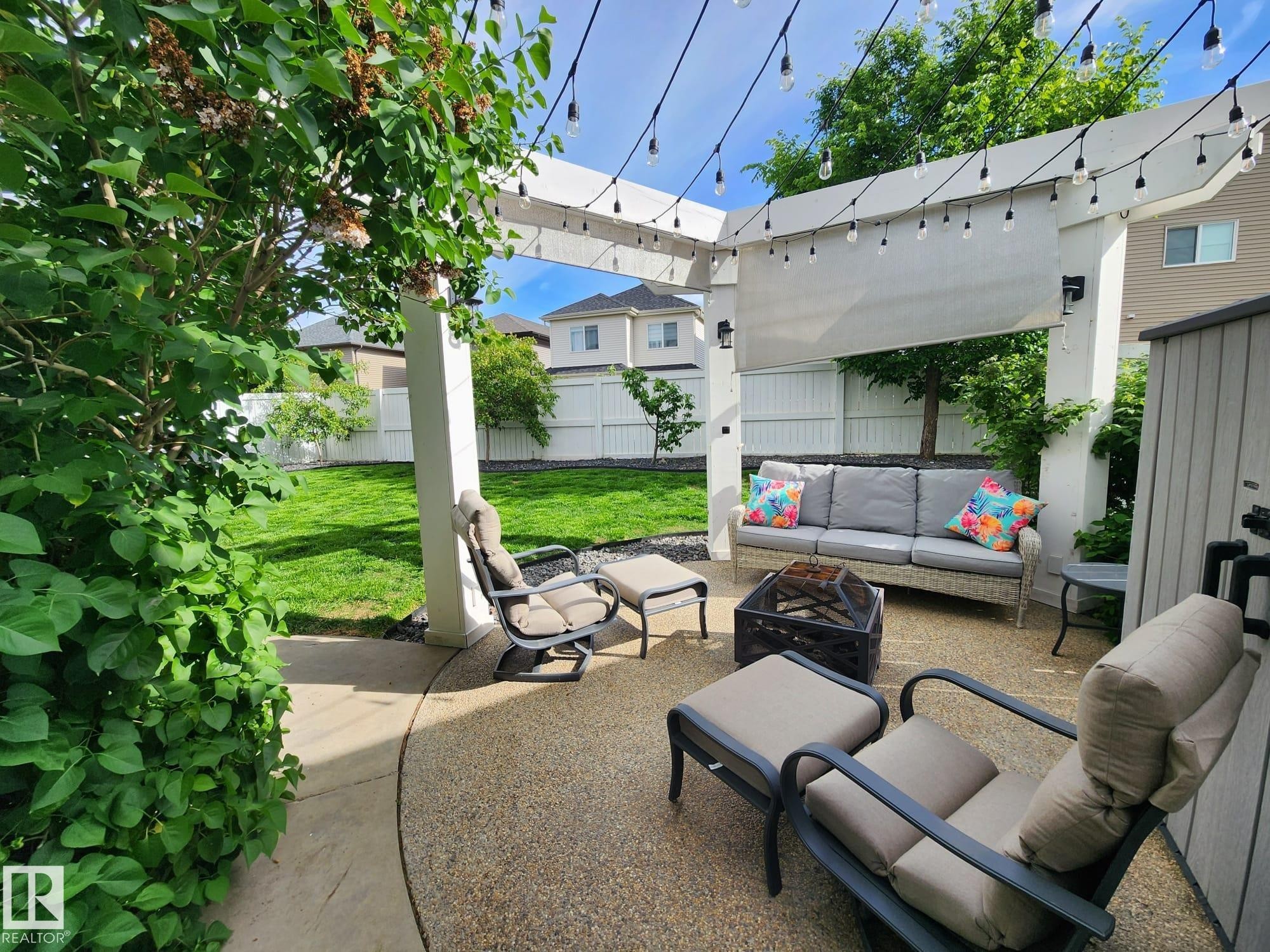 Expansive patio featuring a white pergola structure with string lighting, a concrete aggregate surface, and a retractable sunshade - 22933 94A Avenue, Edmonton, AB - Outdoor With Deck Patio Veranda