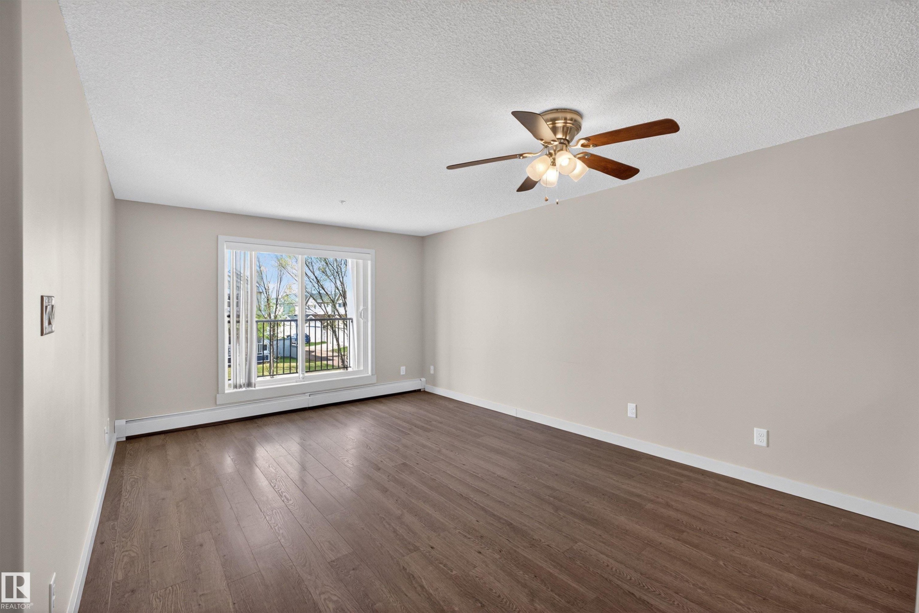 Spacious room featuring wood-finish flooring, a contemporary ceiling fan with lighting, and neutral wall tones - 215 6084 Stanton Drive, Edmonton, AB - Indoor Photo Showing Other Room