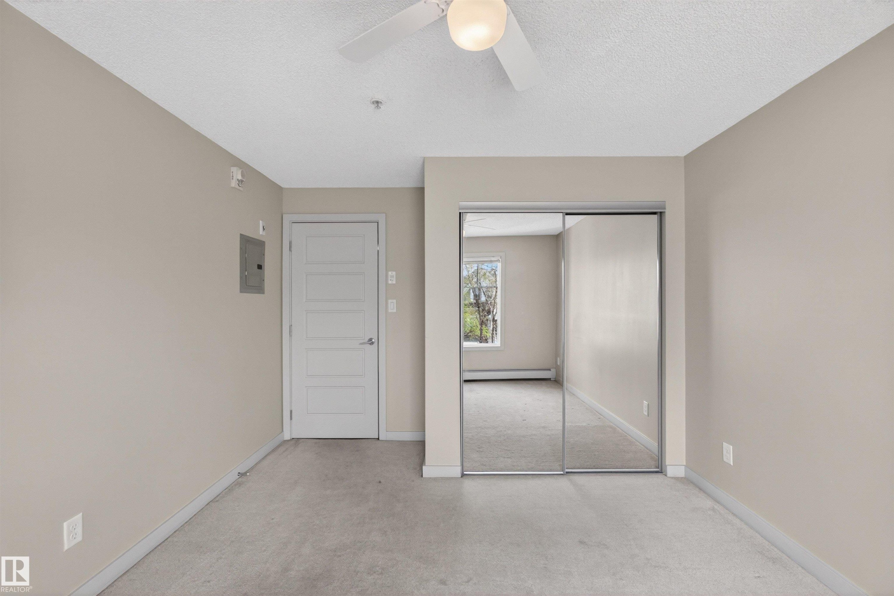 Carpeted interior space featuring a ceiling fan with integrated lighting, a paneled door, and a mirrored closet - 215 6084 Stanton Drive, Edmonton, AB - Indoor Photo Showing Other Room