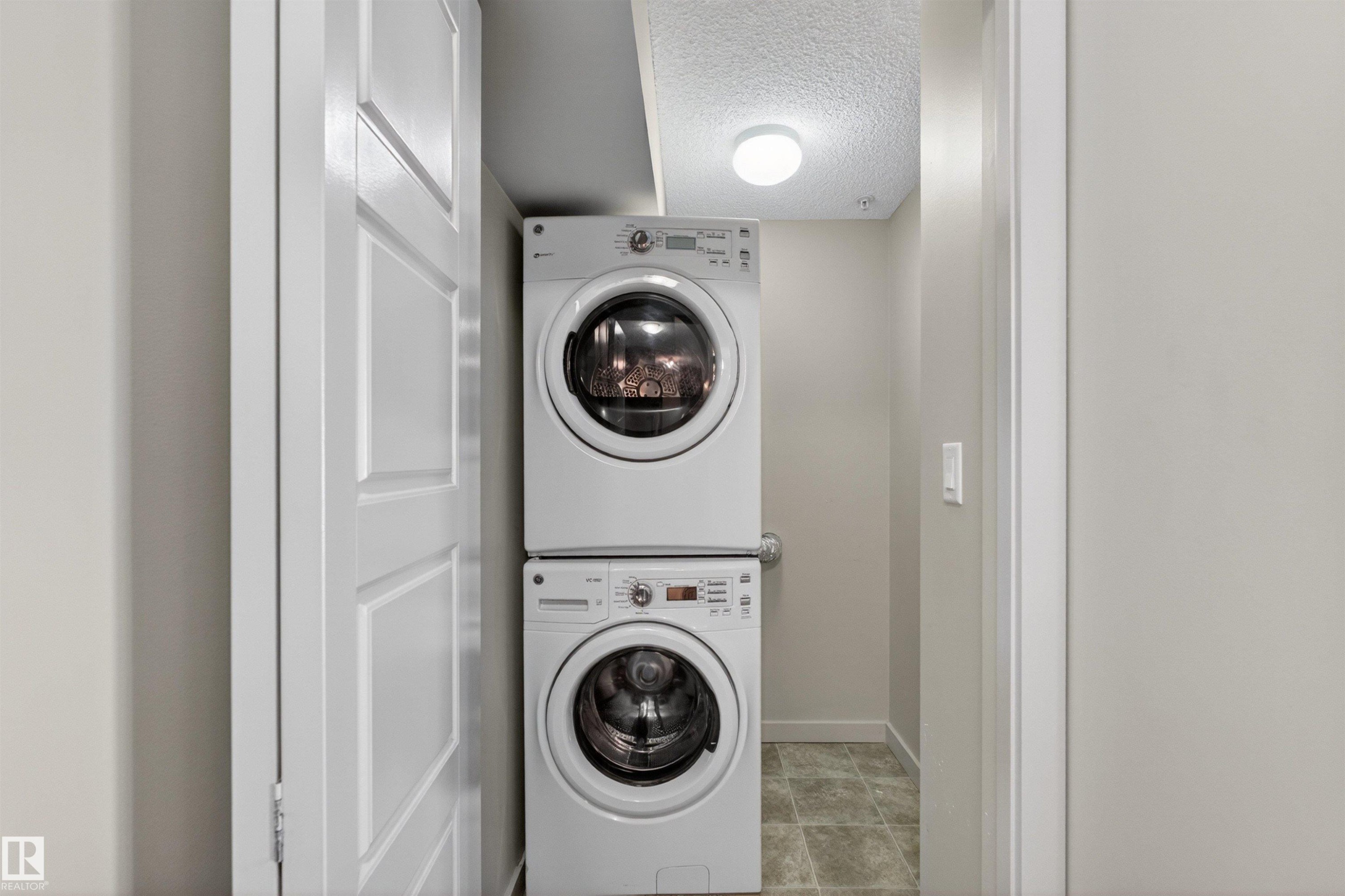 Dedicated laundry area featuring a stacked washer and dryer unit, overhead lighting, and tiled flooring - 215 6084 Stanton Drive, Edmonton, AB - Indoor Photo Showing Laundry Room