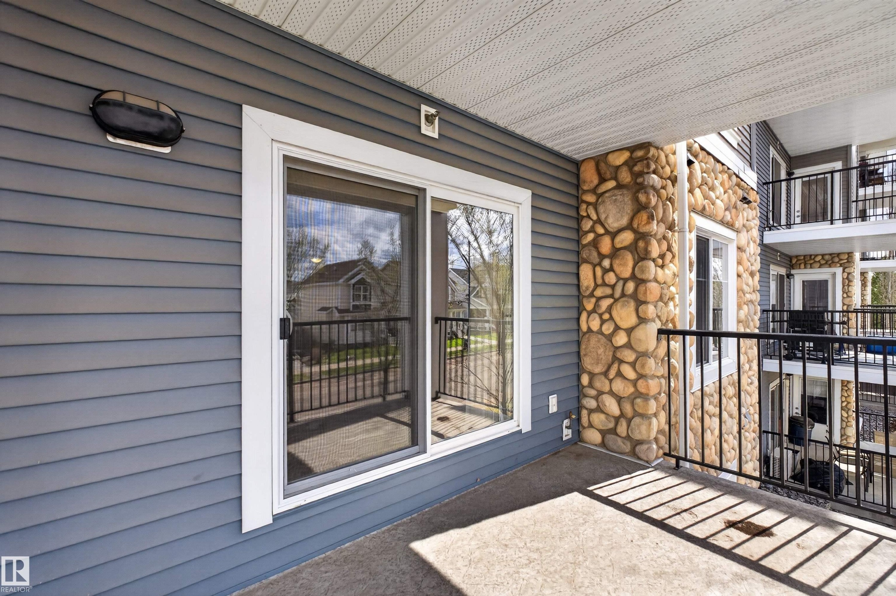 Outdoor patio featuring a sliding glass door entry, stone accent pillar, and black metal railing - 215 6084 Stanton Drive, Edmonton, AB - Outdoor With Balcony With Exterior