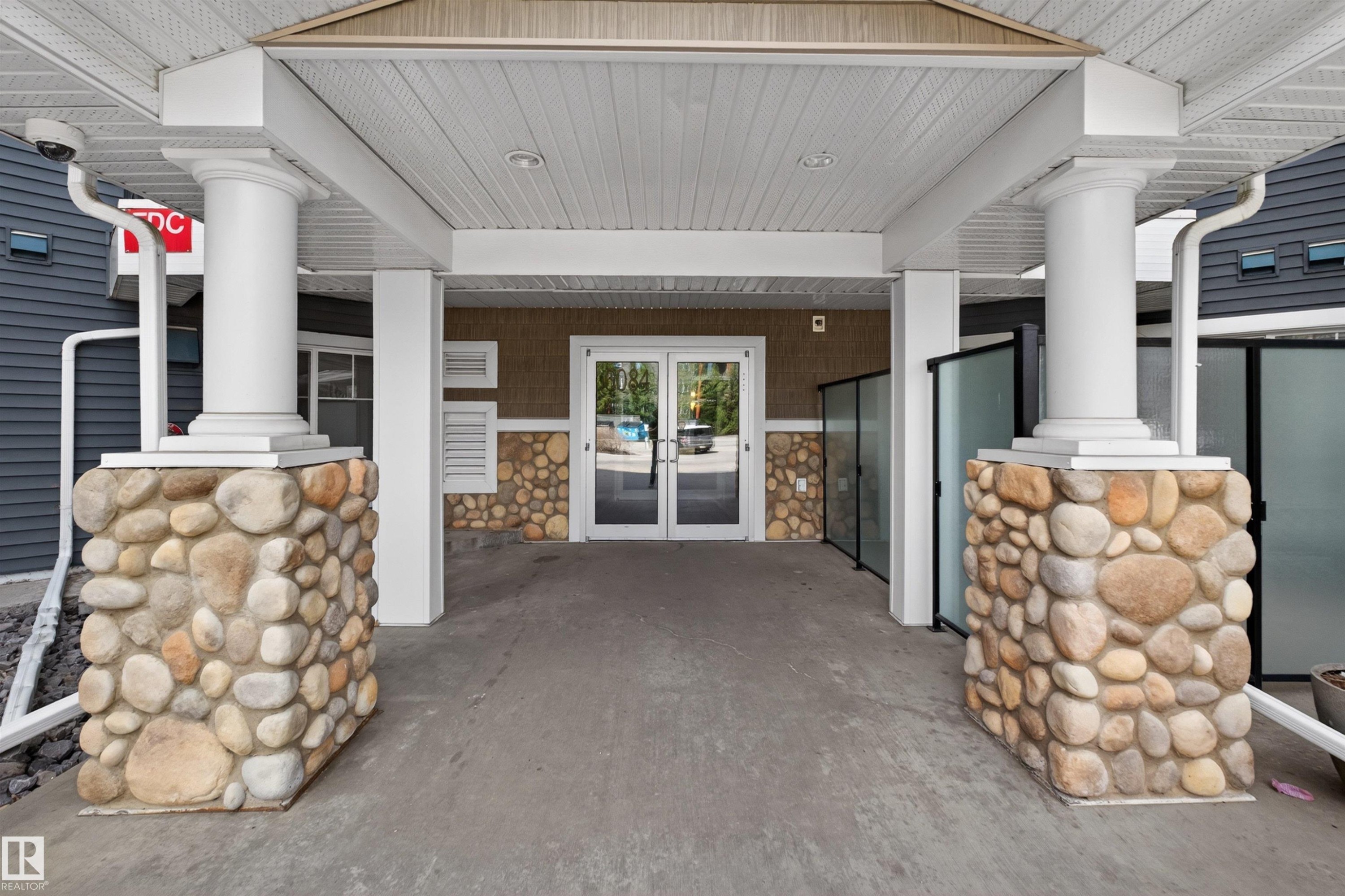 Covered entryway featuring large stone-clad columns supporting white fluted pillars - 215 6084 Stanton Drive, Edmonton, AB -