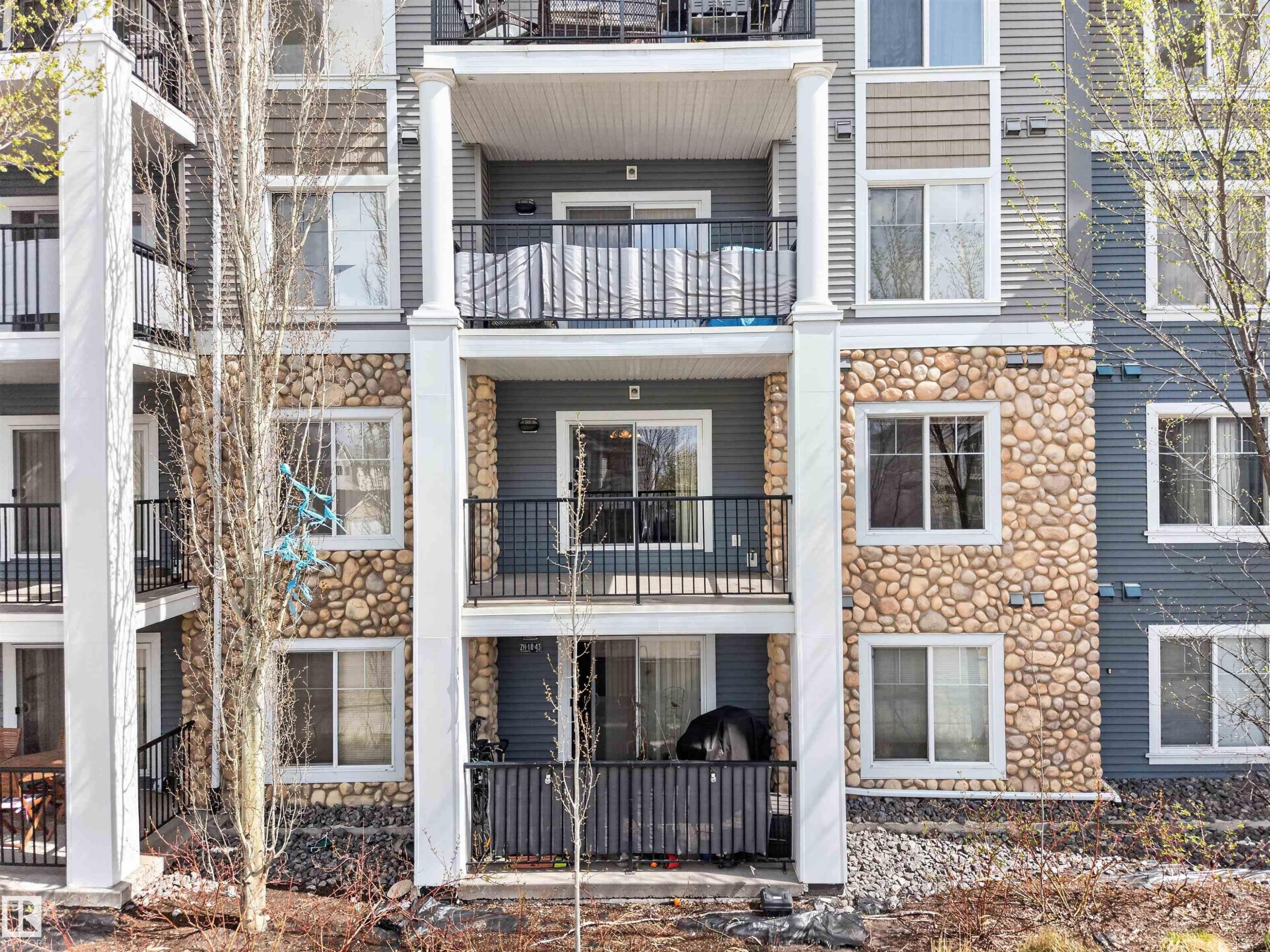 Multi-story residential facade featuring stone veneer accents, white balustrades, and private balconies with black railings - 215 6084 Stanton Drive, Edmonton, AB - Outdoor With Balcony With Facade