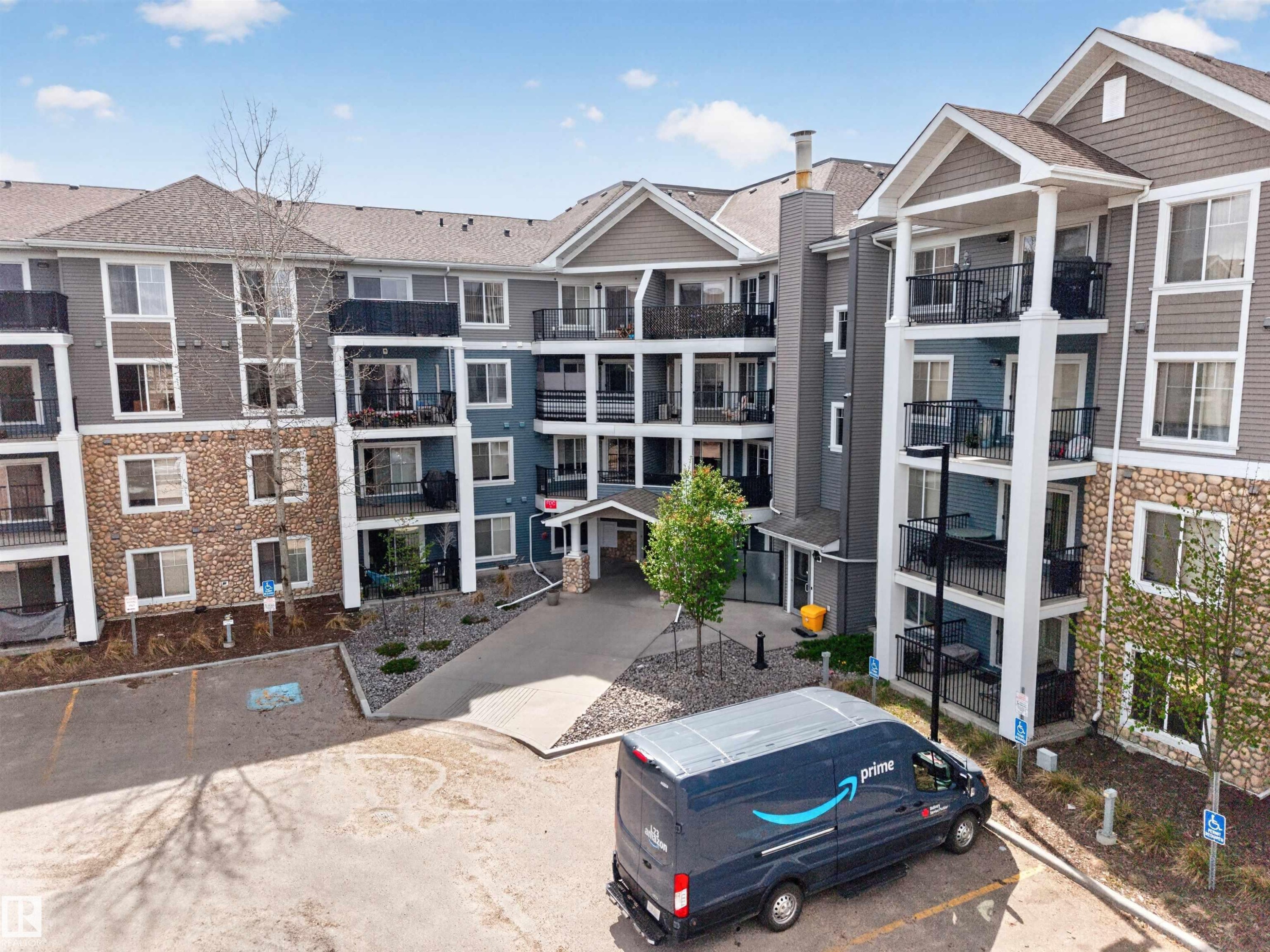 Multi-story residential building featuring stone and siding exterior, private balconies, and a paved parking area - 215 6084 Stanton Drive, Edmonton, AB - Outdoor With Facade
