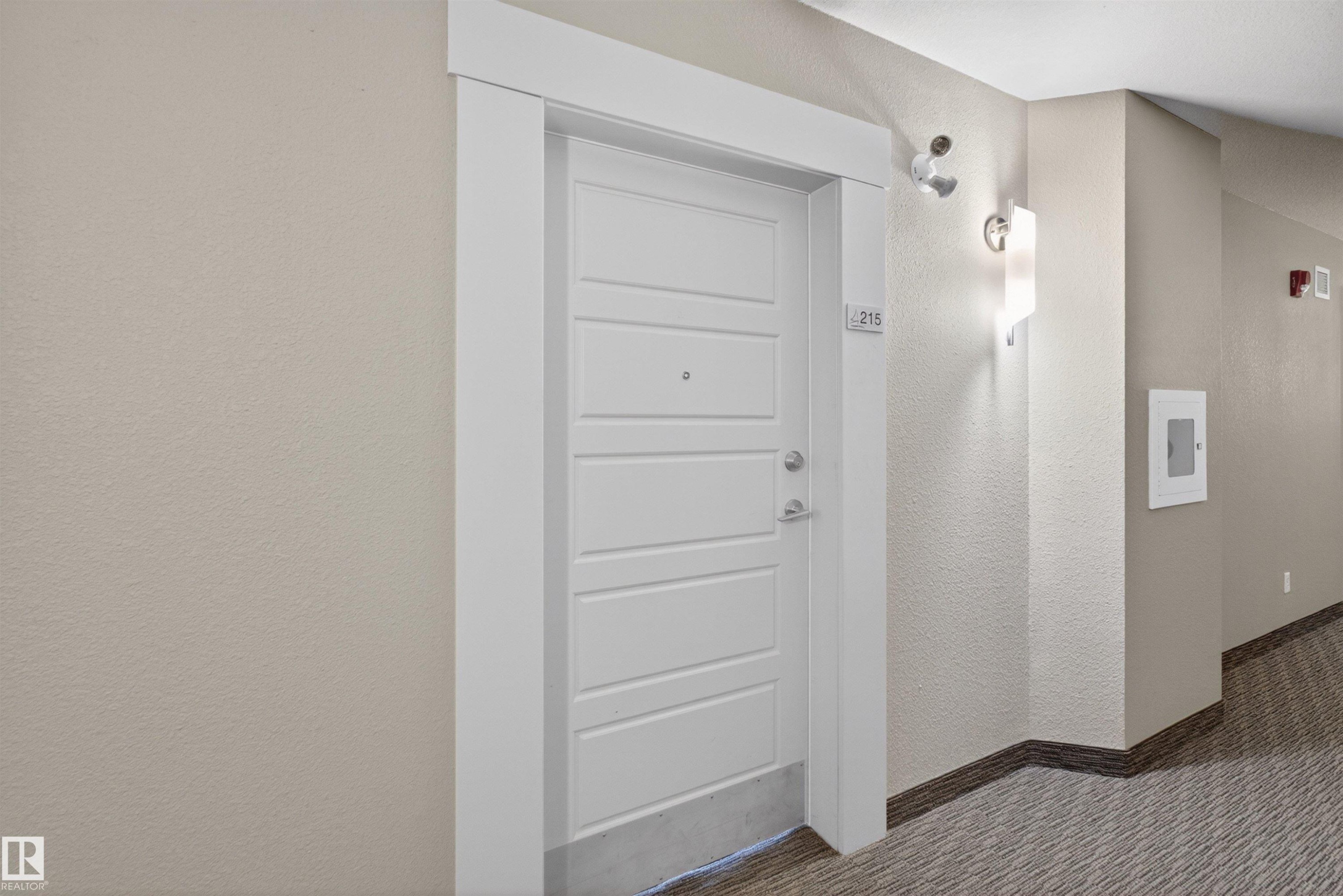 Entry door with horizontal paneling, crisp white trim, and brushed nickel hardware - 215 6084 Stanton Drive, Edmonton, AB - Indoor Photo Showing Other Room