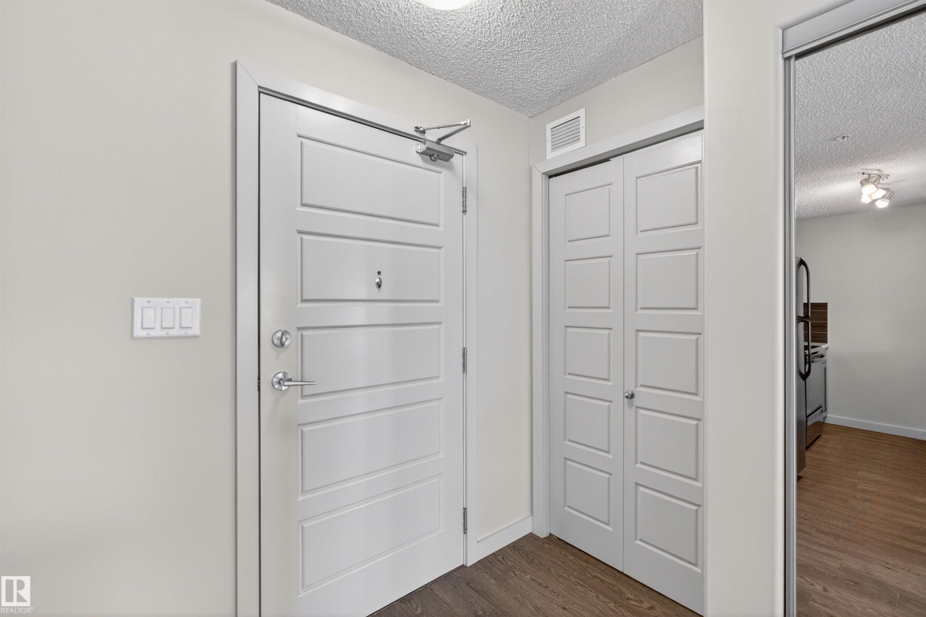 Entryway featuring a paneled door with polished chrome hardware, an overhead door closer, and light wood-finish flooring - 215 6084 Stanton Drive, Edmonton, AB - Indoor Photo Showing Other Room
