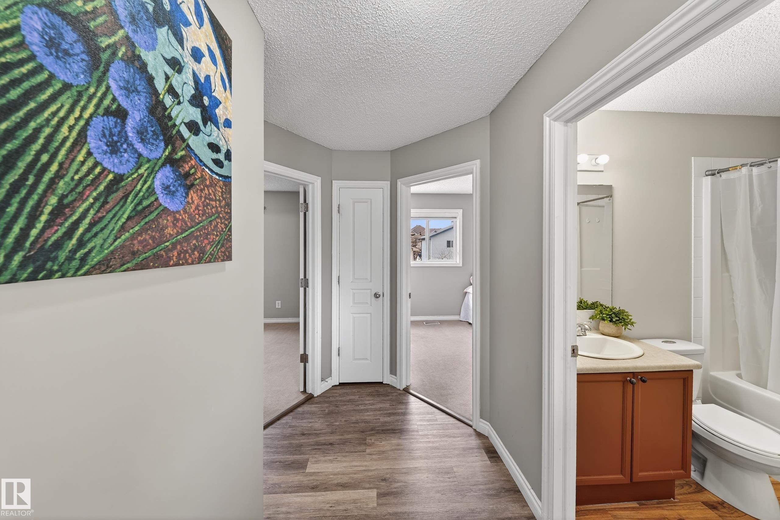 This property features wood-look flooring throughout the hallway and into the visible bathroom, which includes a white vanity with a light-colored countertop and a white toilet - 3517 25 Street, Edmonton, AB - Indoor Photo Showing Other Room