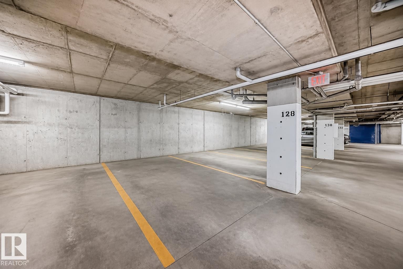 Parking garage featuring concrete walls, concrete flooring with painted yellow lines, and exposed overhead piping - 327 508 Griesbach Parade, Edmonton, AB - Indoor Photo Showing Garage