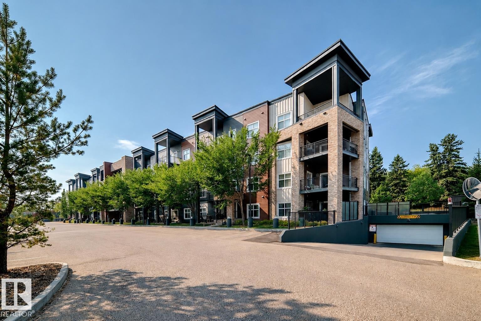 Contemporary multi-story building featuring a brick and panel facade, multiple private balconies with dark railings, and a secure underground parking garage entrance - 327 508 Griesbach Parade, Edmonton, AB - Outdoor With Balcony