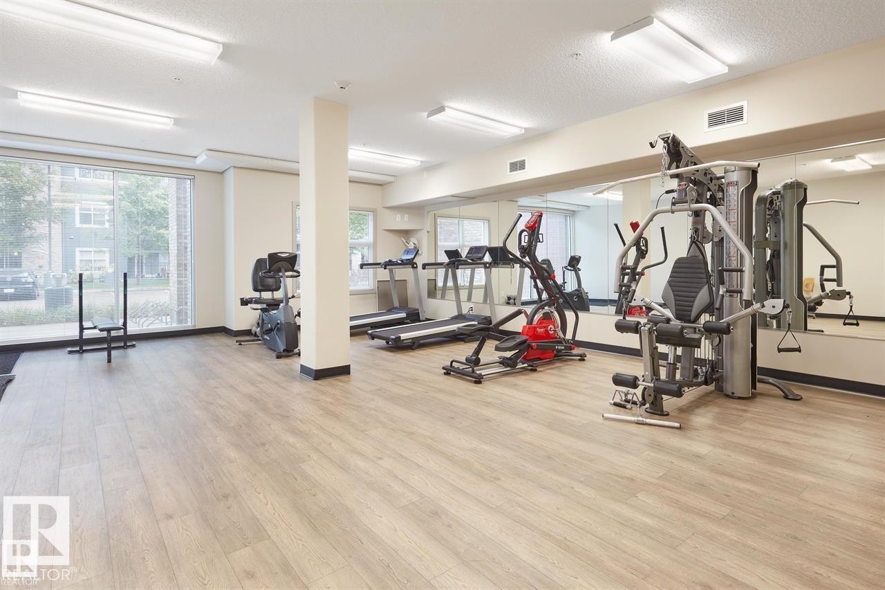 Fitness room featuring wood-finish flooring, mirrored wall, large windows, and overhead fluorescent lighting - 327 508 Griesbach Parade, Edmonton, AB - Indoor Photo Showing Gym Room