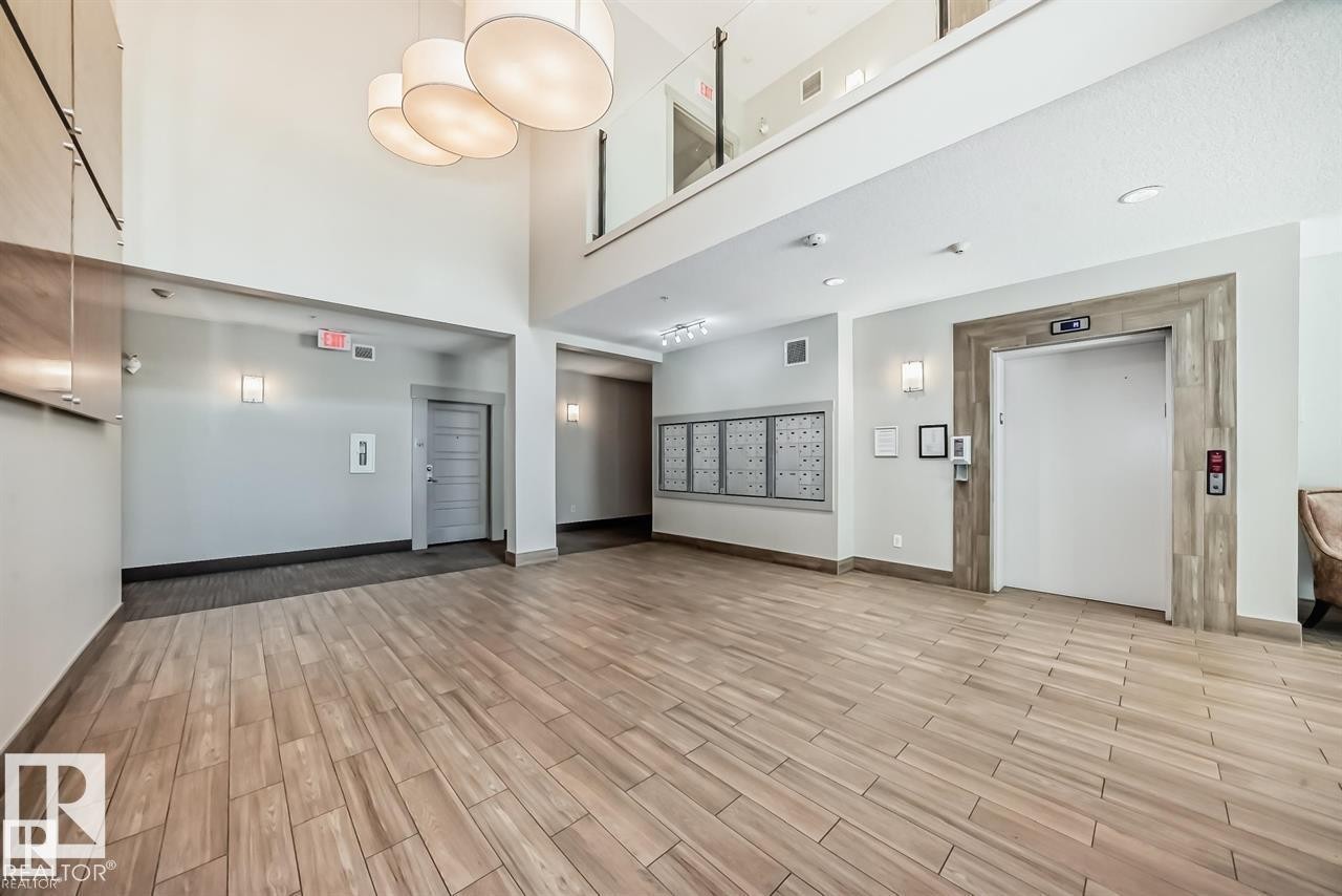 Spacious lobby featuring wood-finish flooring, high ceilings, and contemporary pendant lighting - 327 508 Griesbach Parade, Edmonton, AB - Indoor Photo Showing Other Room