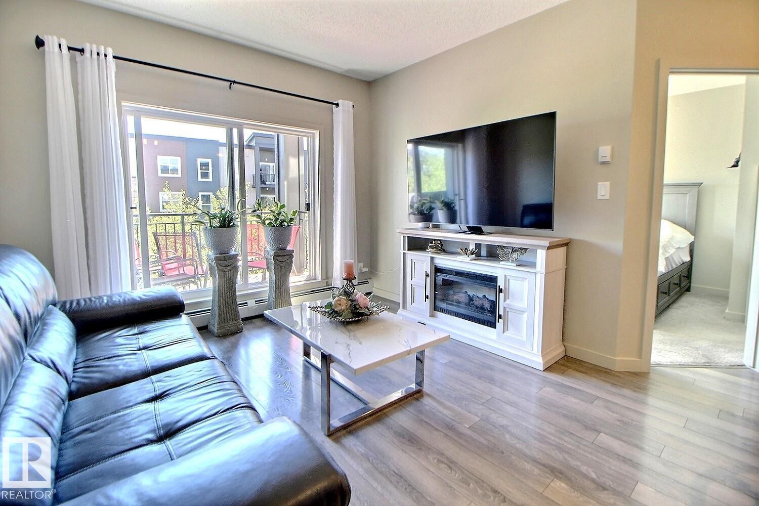 Living area featuring light wood-finish flooring and a built-in electric fireplace media console - 327 508 Griesbach Parade, Edmonton, AB - Indoor Photo Showing Living Room With Fireplace
