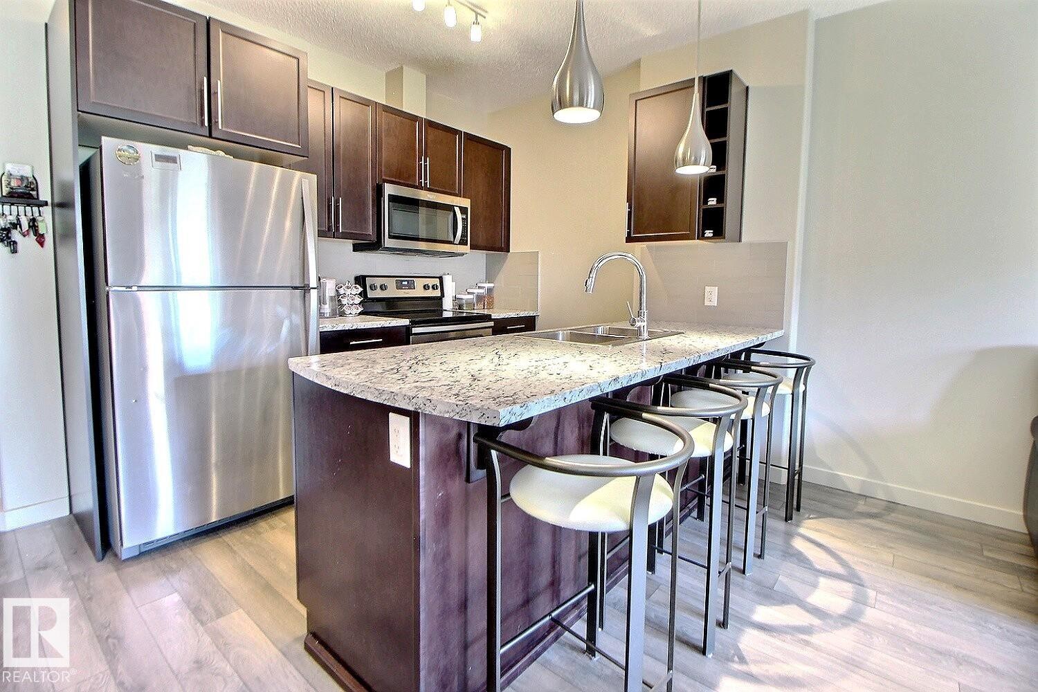 Kitchen featuring an expansive island with a granite countertop, undermount sink, and pendant lighting - 327 508 Griesbach Parade, Edmonton, AB - Indoor Photo Showing Kitchen With Stainless Steel Kitchen With Double Sink With Upgraded Kitchen