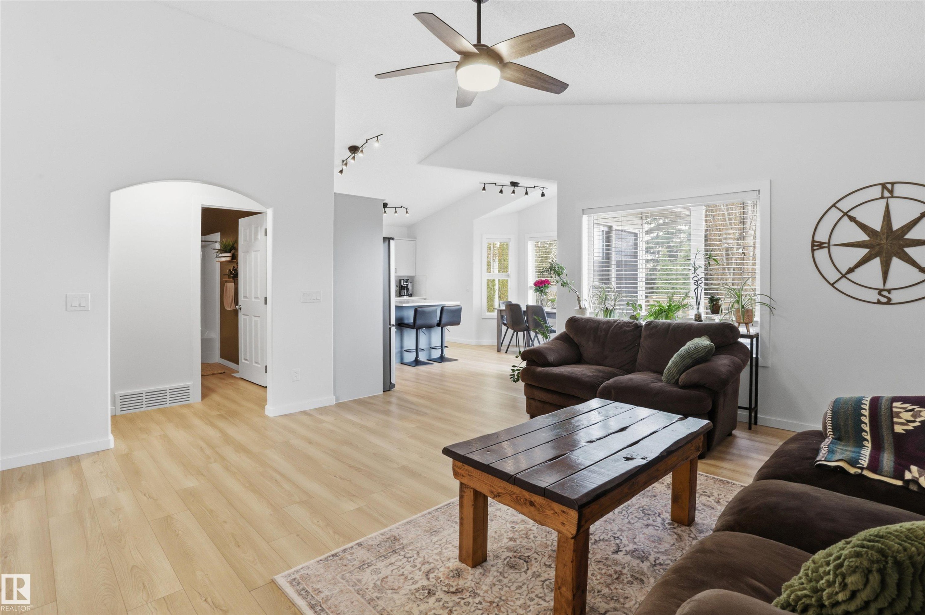 Vaulted ceiling living area featuring wood-finish flooring, a ceiling fan, and large windows - 396 Kananaskis Way, Devon, AB - Indoor Photo Showing Living Room