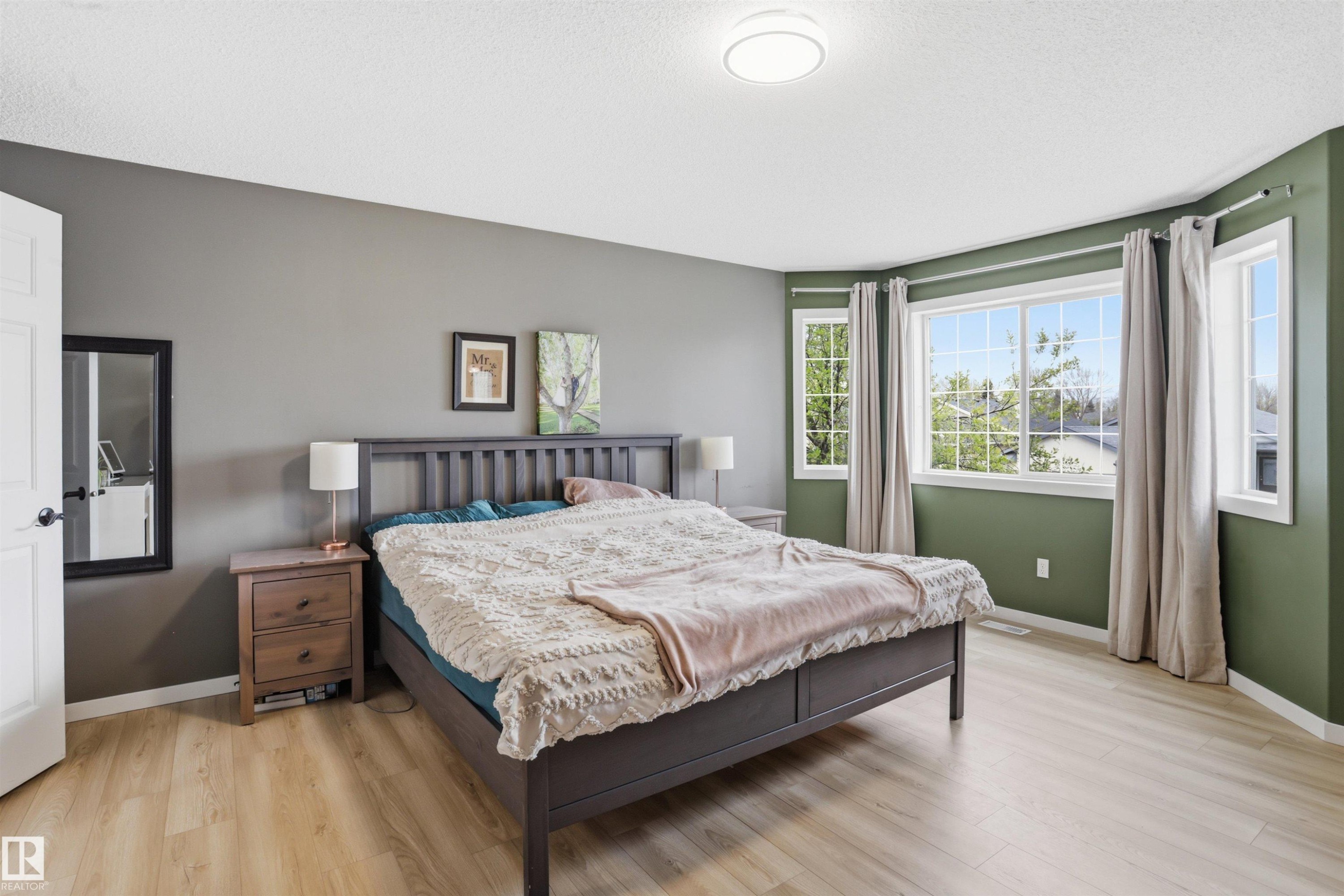 Spacious room featuring light wood-finish flooring, a contemporary ceiling light fixture, and large windows with privacy drapes - 396 Kananaskis Way, Devon, AB - Indoor Photo Showing Bedroom