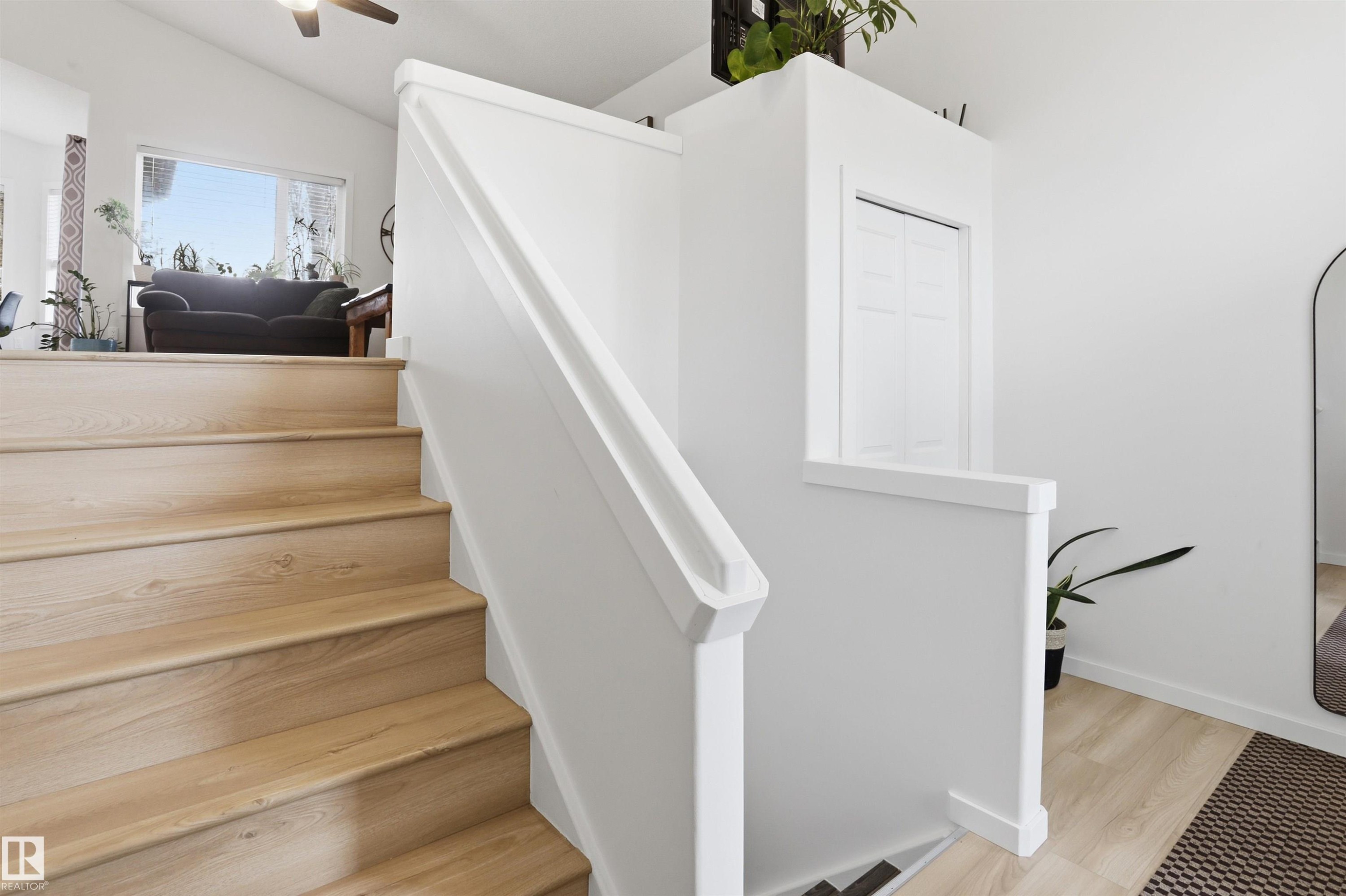 Staircase featuring wood-finish treads and white risers, leading to an upper level with a vaulted ceiling and large windows - 396 Kananaskis Way, Devon, AB - Indoor Photo Showing Other Room