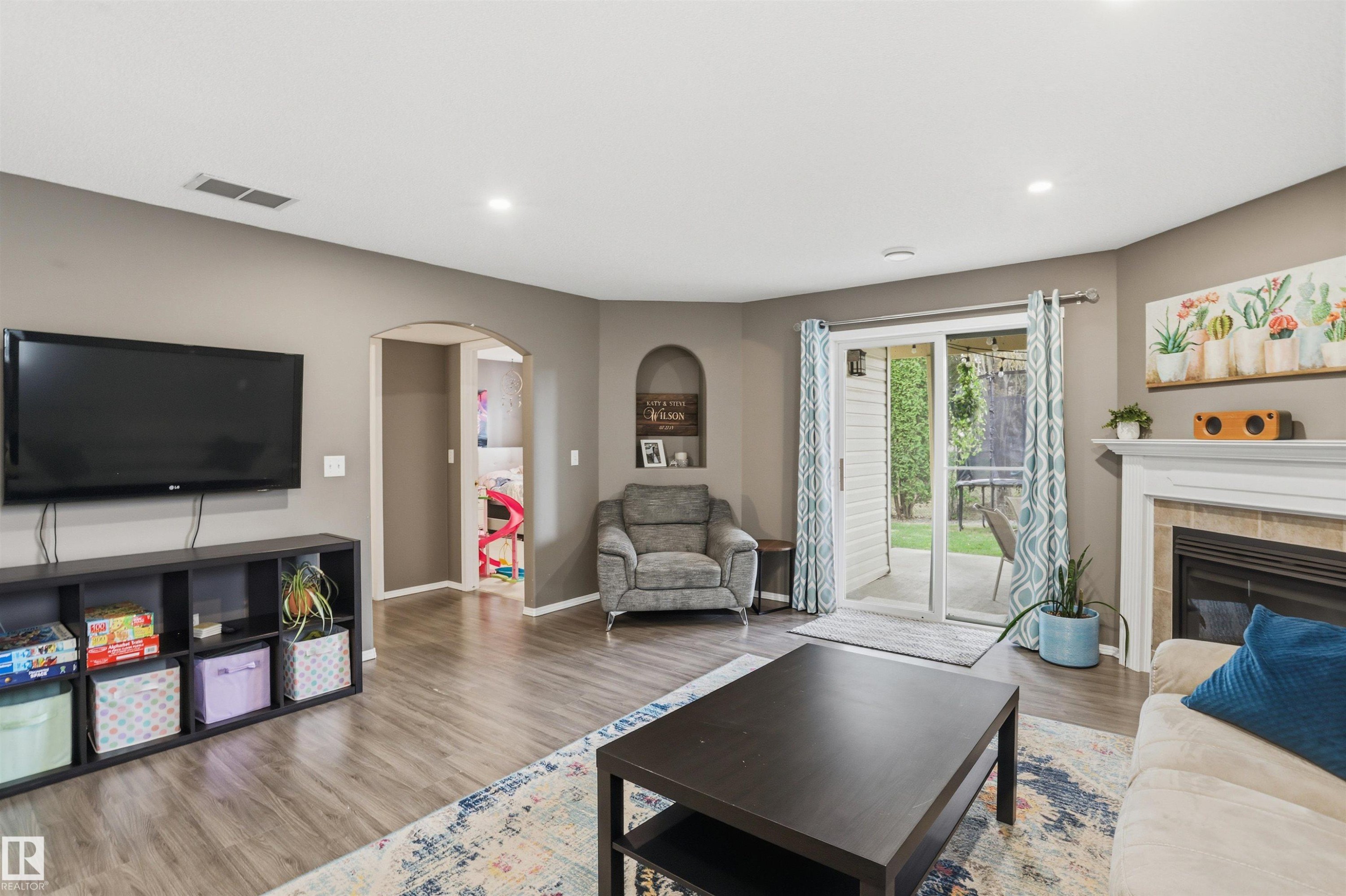Spacious living area featuring wood-finish flooring, recessed lighting, and a fireplace with a tile surround and white mantel - 396 Kananaskis Way, Devon, AB - Indoor Photo Showing Living Room With Fireplace