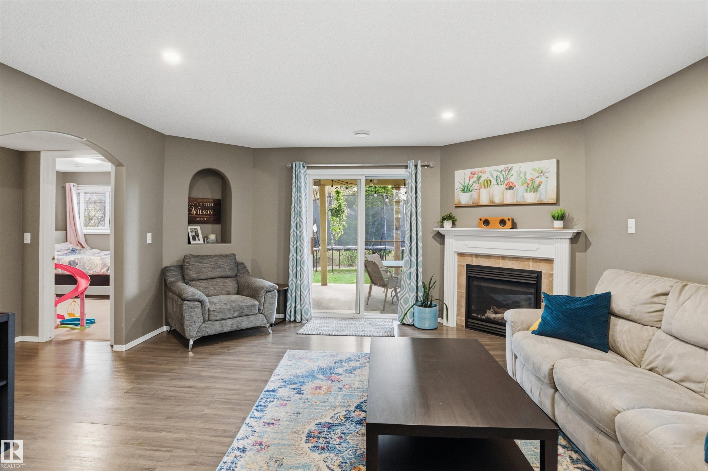 Spacious living area featuring wood-finish flooring, recessed lighting, and a fireplace with a white mantel and tile surround - 396 Kananaskis Way, Devon, AB - Indoor Photo Showing Living Room With Fireplace