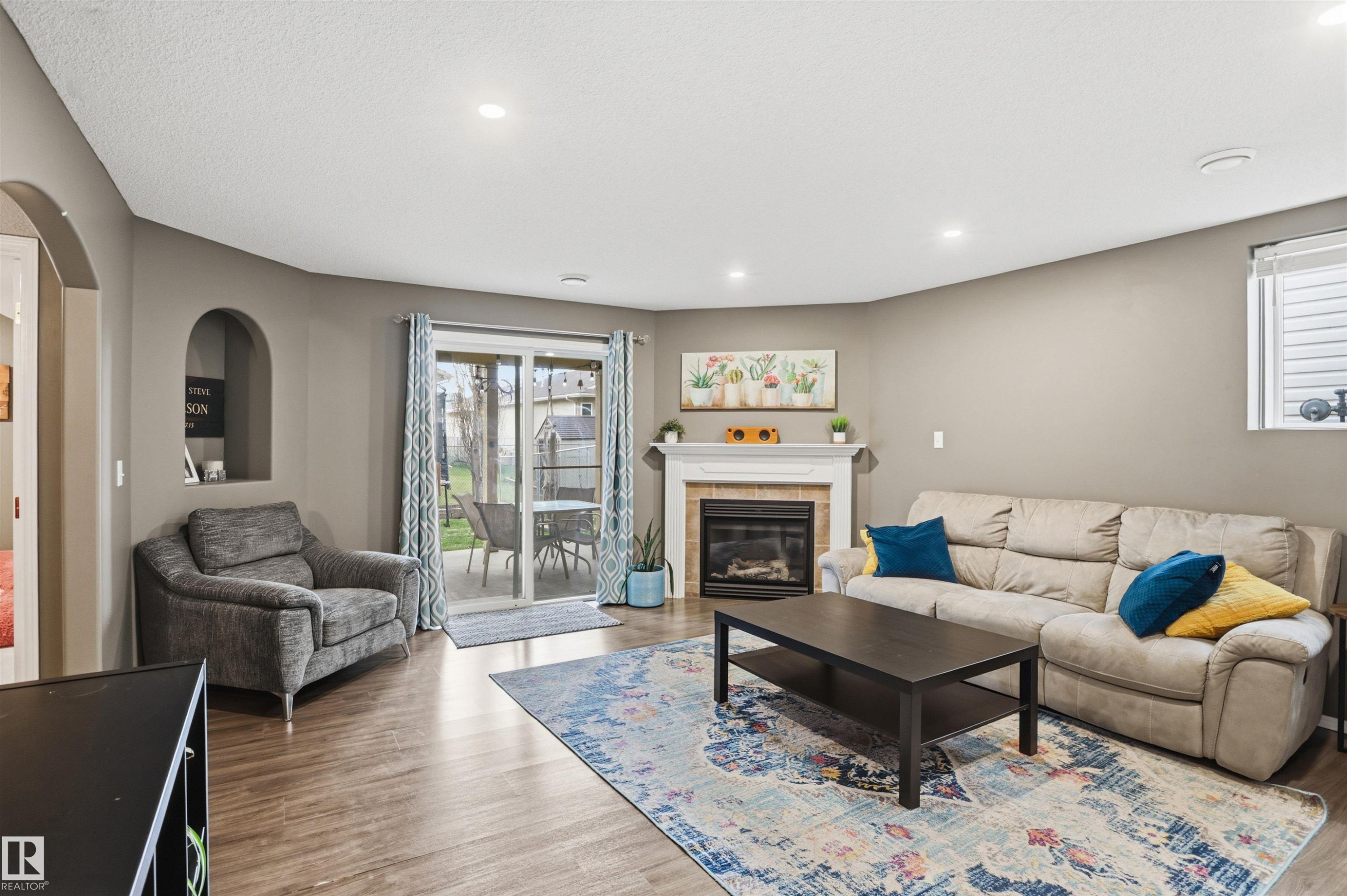 Living area featuring wood-finish flooring, a fireplace with a white mantel, recessed lighting, and a sliding glass door leading to the exterior - 396 Kananaskis Way, Devon, AB - Indoor Photo Showing Living Room With Fireplace