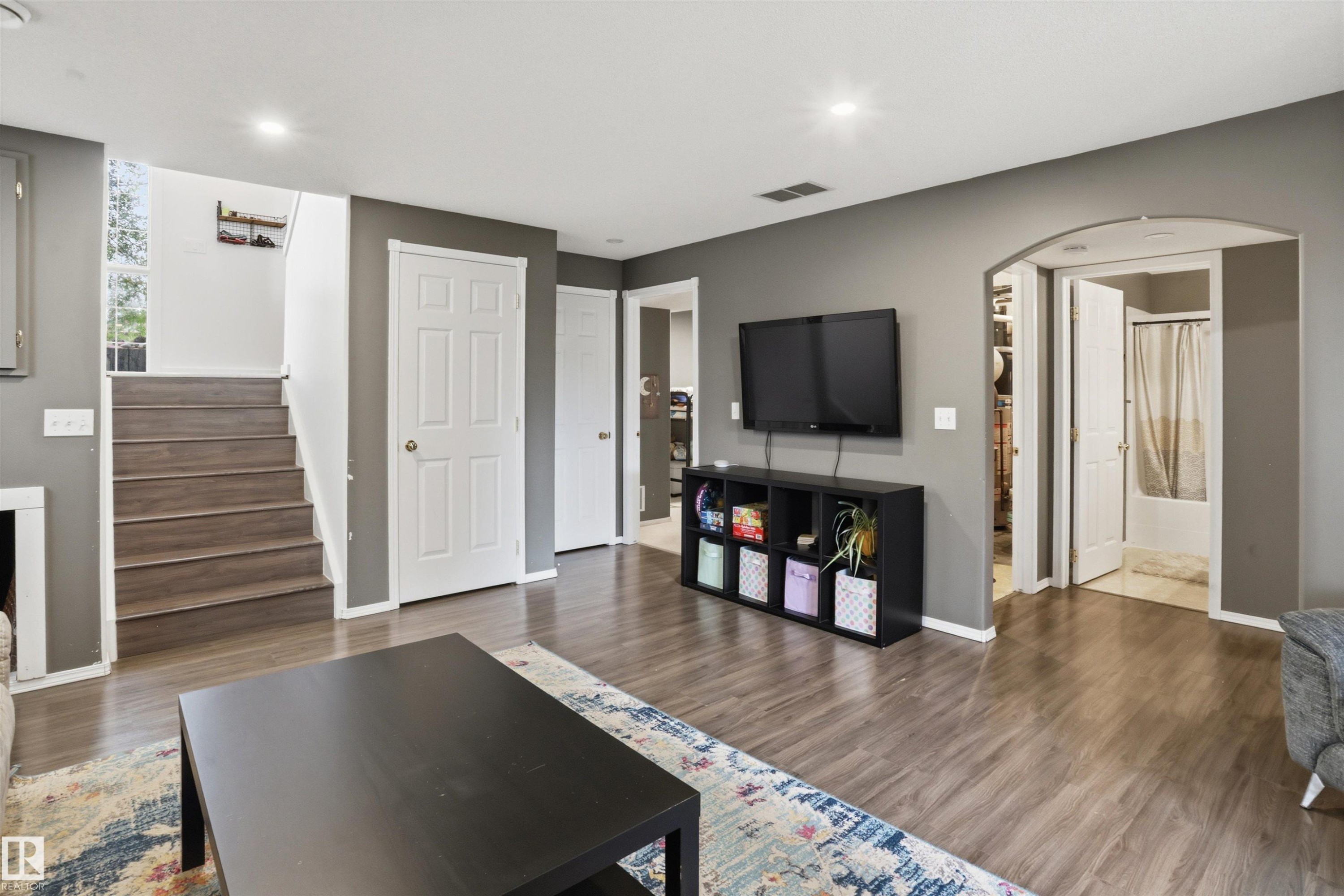 Open concept interior featuring wood-finish flooring, recessed lighting, a white six-panel door, and an arched entry - 396 Kananaskis Way, Devon, AB - Indoor Photo Showing Other Room